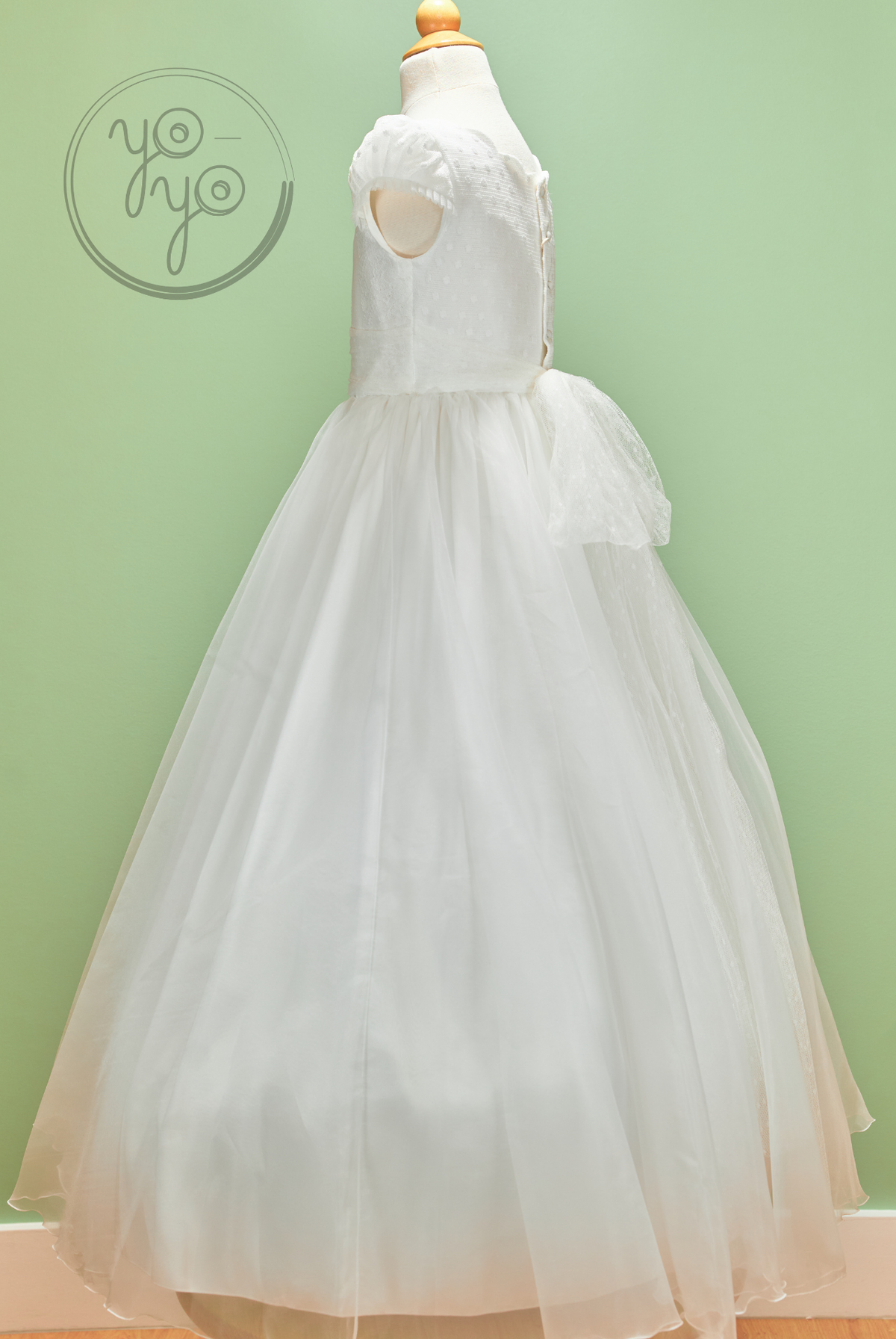 White Iris Dress on a mannequin with a sleeveless textured bodice, full embroidered tulle skirt, and a sheer back waist bow.
