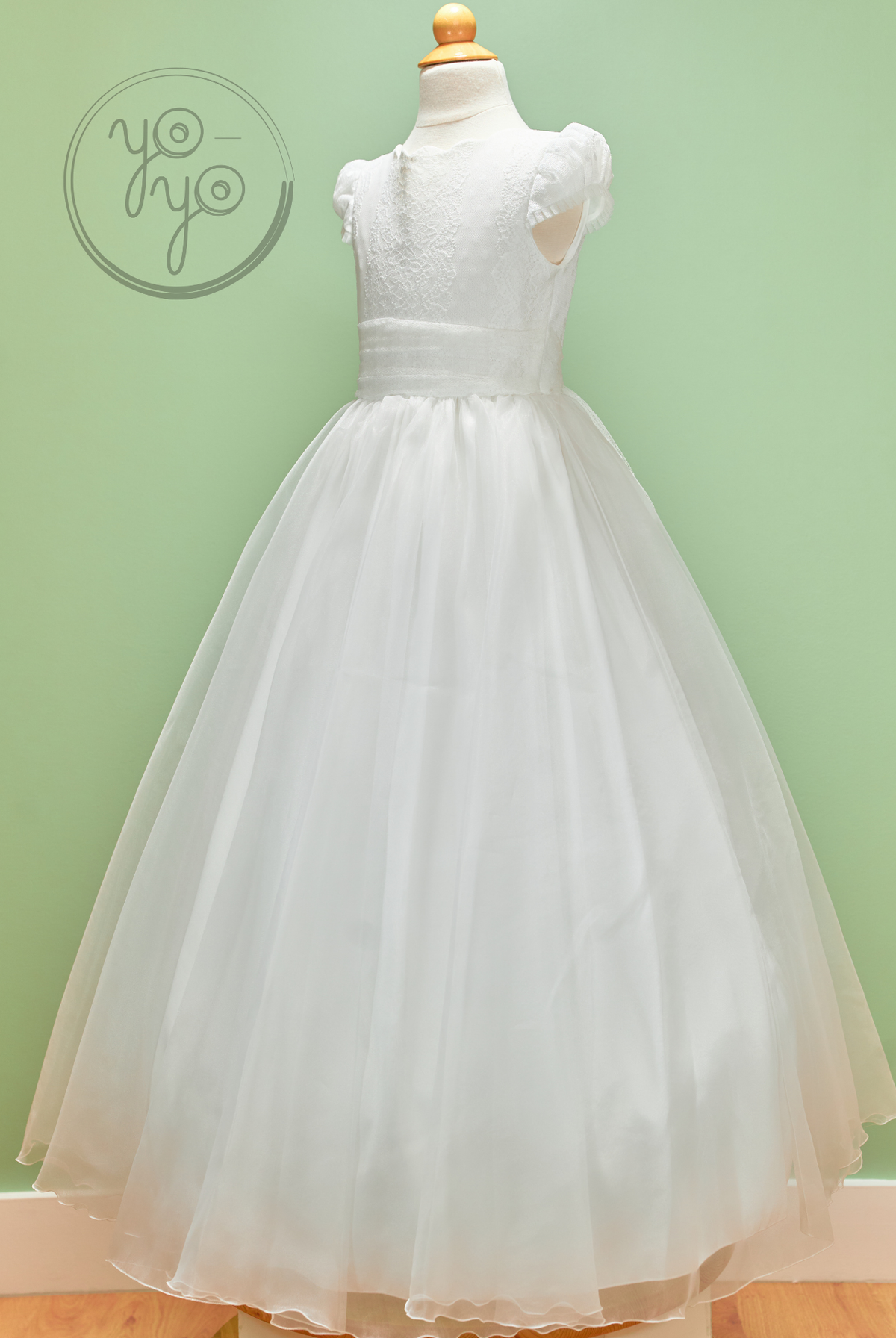 YoYo Boutique Iris Dress: a white sleeveless First Communion dress on a mannequin, featuring an embroidered tulle bodice, satin waistband, and skirt.