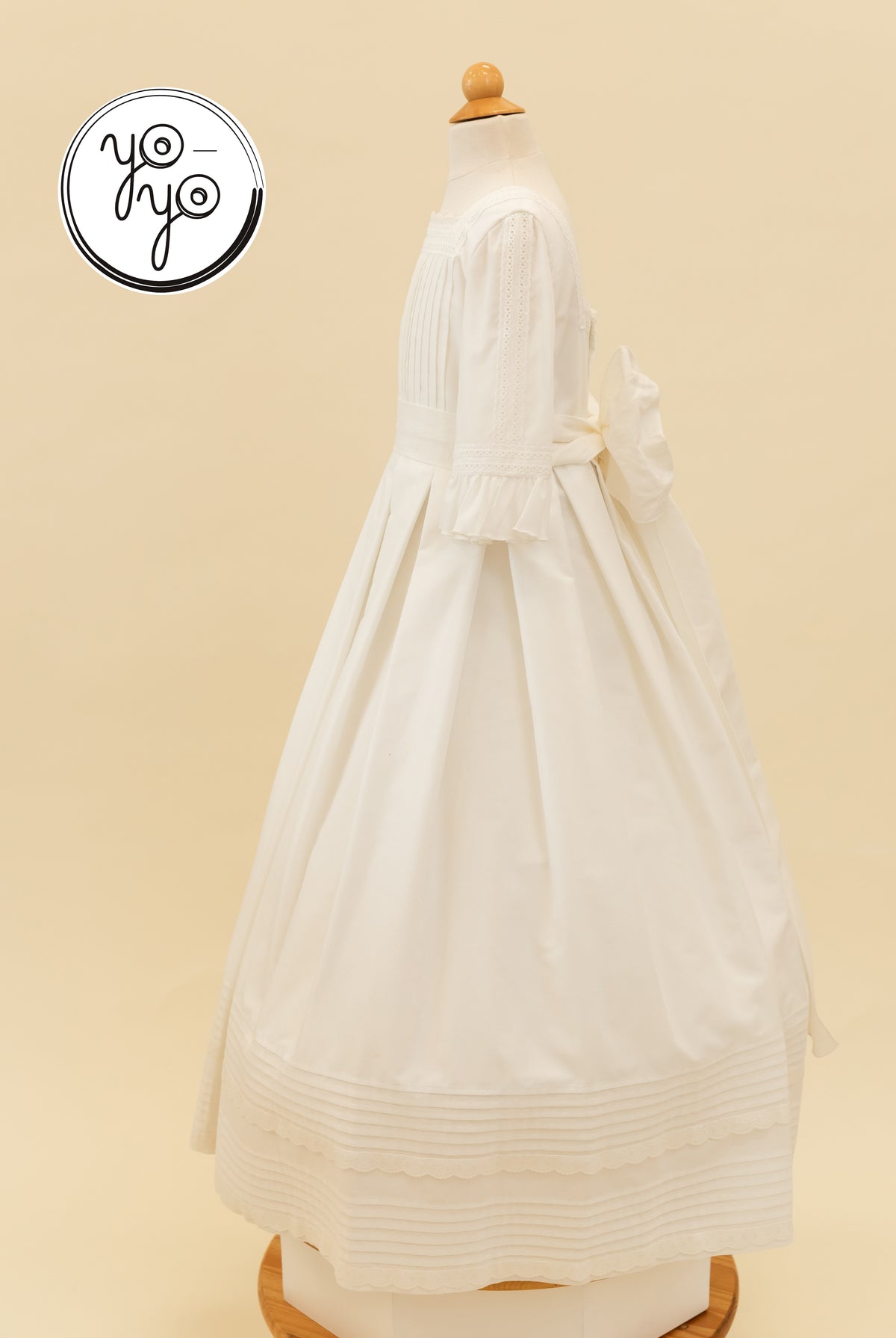 Side view of the white Claudine Dress by YoYo Boutique, featuring pleats, three-quarter ruffled sleeves, and a large waist bow.