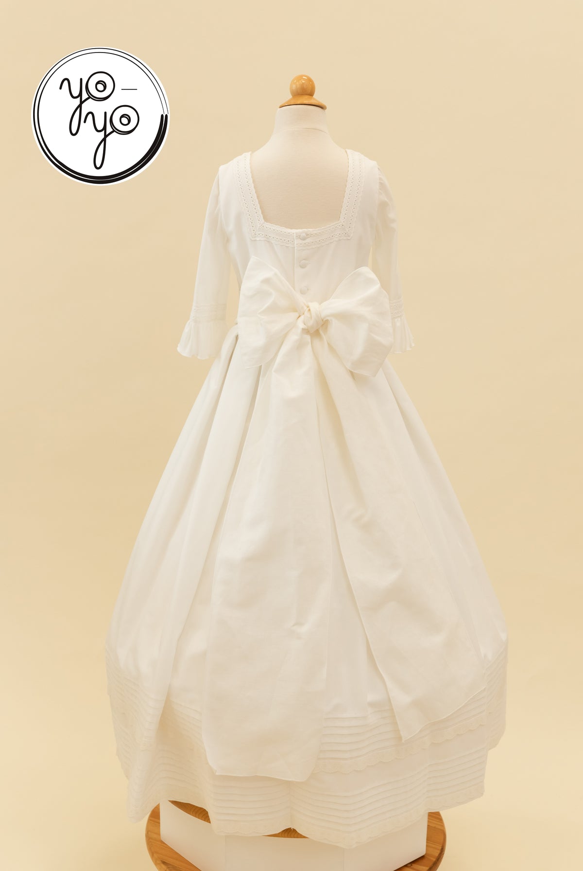 Back view of the cream Claudine Dress featuring a square neckline, three-quarter ruffled sleeves, and a large waist bow.