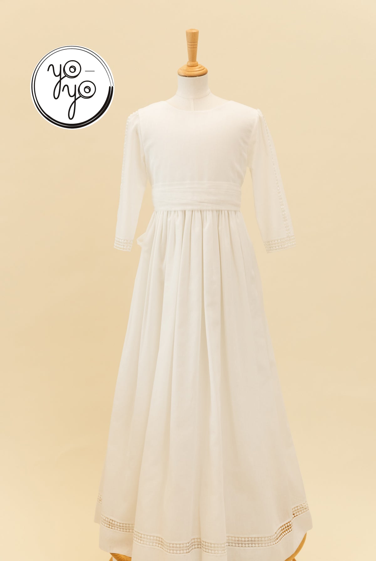 Off-white YoYo Boutique Montserrat dress in linen, floor-length with long sleeves, gathered waist, and delicate lace trim on sleeves and hem.