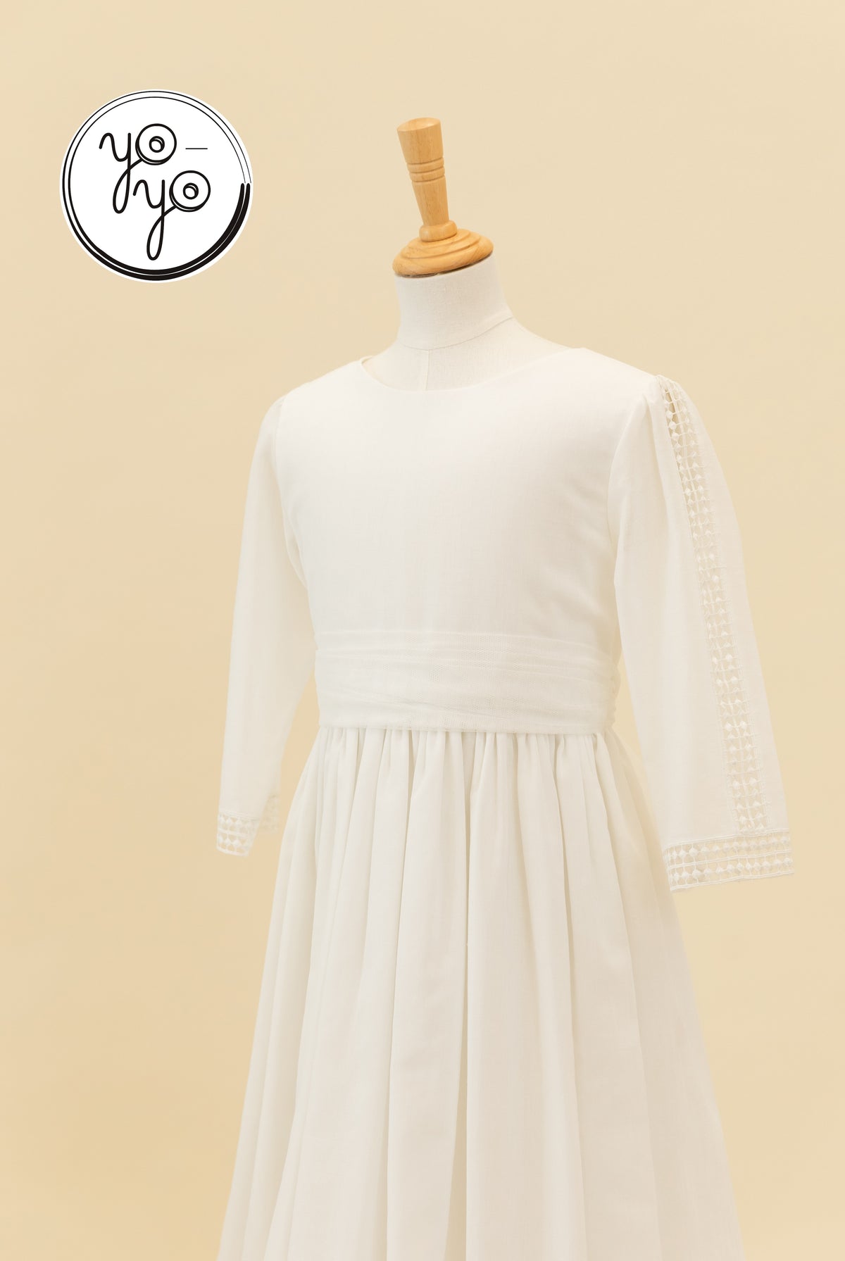 Off-white long-sleeved Montserrat dress on a mannequin, featuring a round neckline, wide waistband, and lace trim on the sleeves.