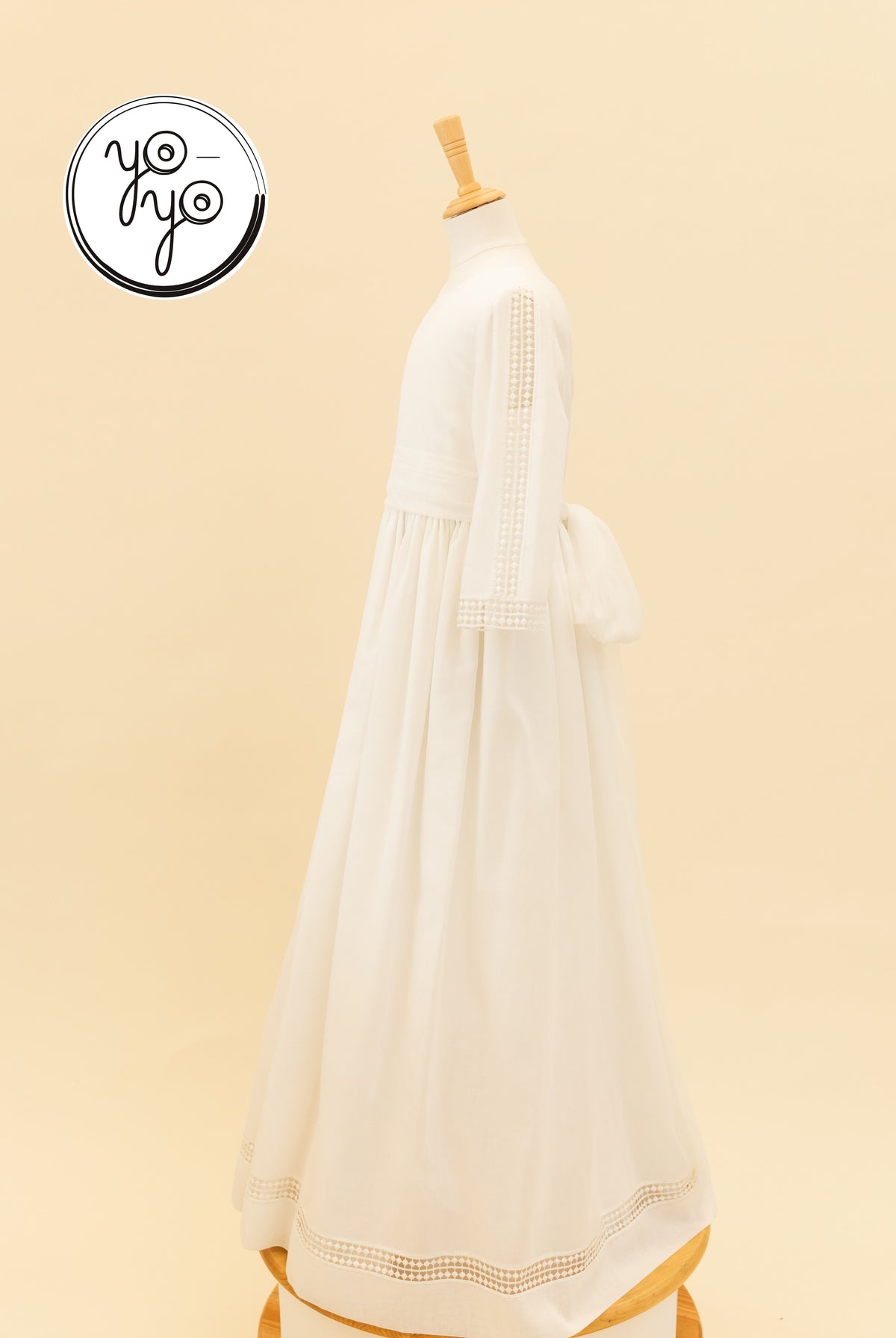 Mannequin wearing a natural white linen Montserrat Dress by YoYo Boutique, featuring lace-trimmed sleeves and hem and a large back bow.