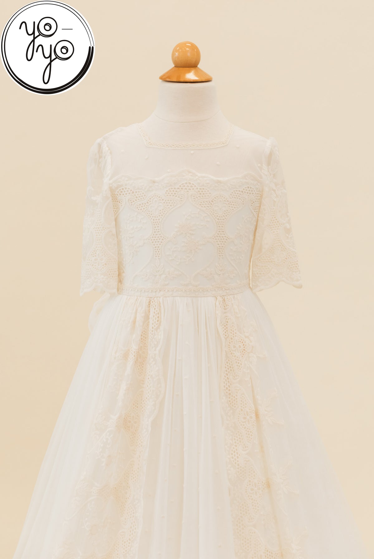 Pino Dress by YoYo Boutique: ivory First Communion dress on a mannequin with a sheer lace bodice, three-quarter sleeves, and a full skirt.