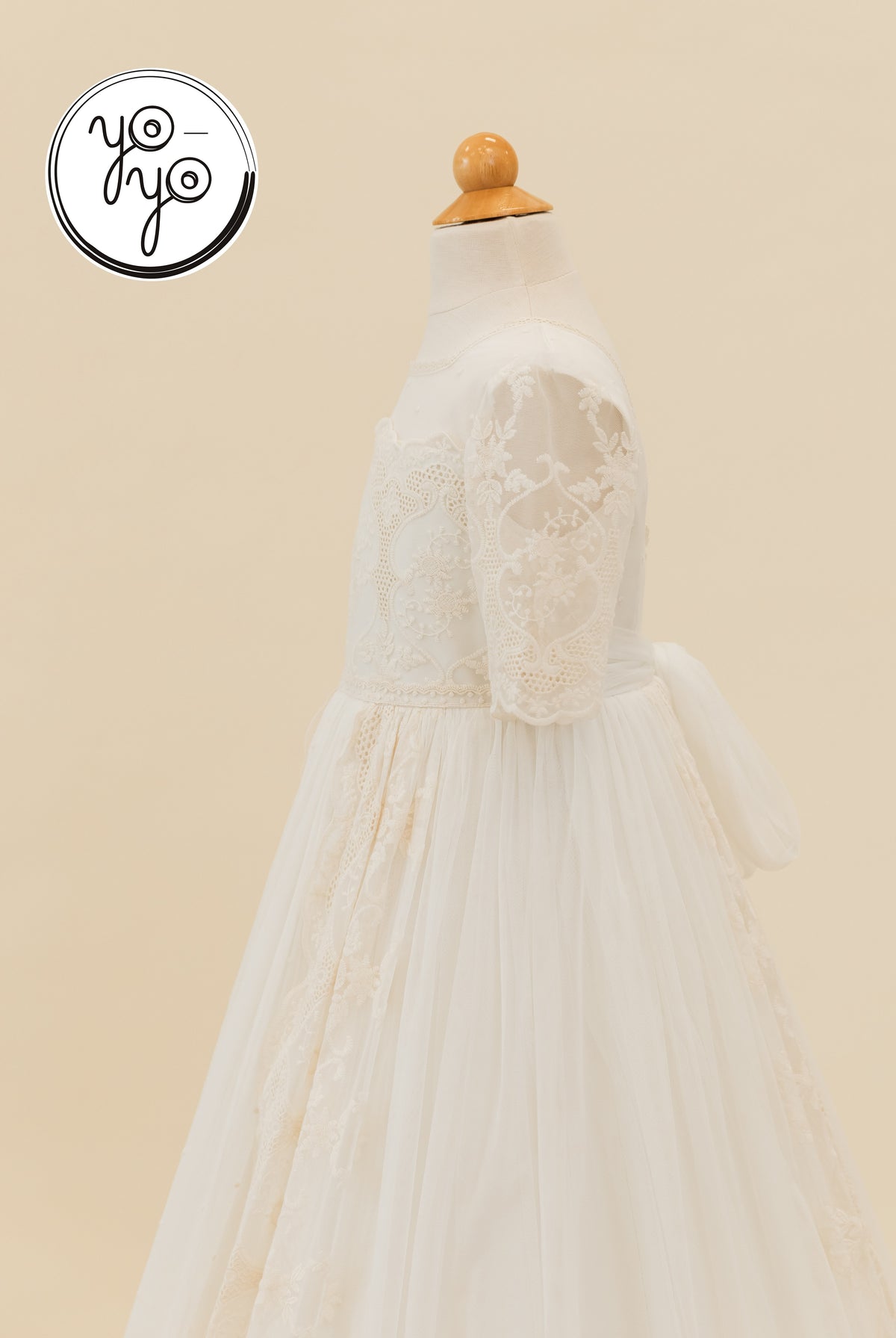 Side view of a tea-length Pino Dress by YoYo Boutique on a mannequin, featuring lace sleeves, an embroidered bodice, and a tulle skirt.