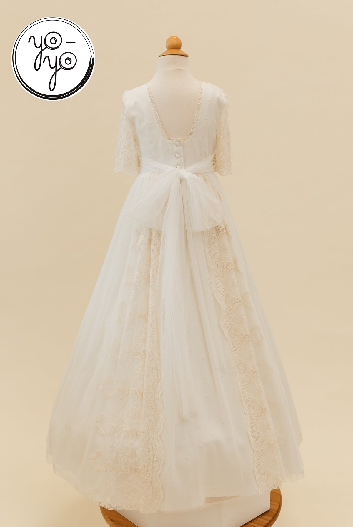 Back view of the cream, floor-length Pino Dress by YoYo Boutique, featuring lace panels, short sleeves, a scooped back, and a waist bow.