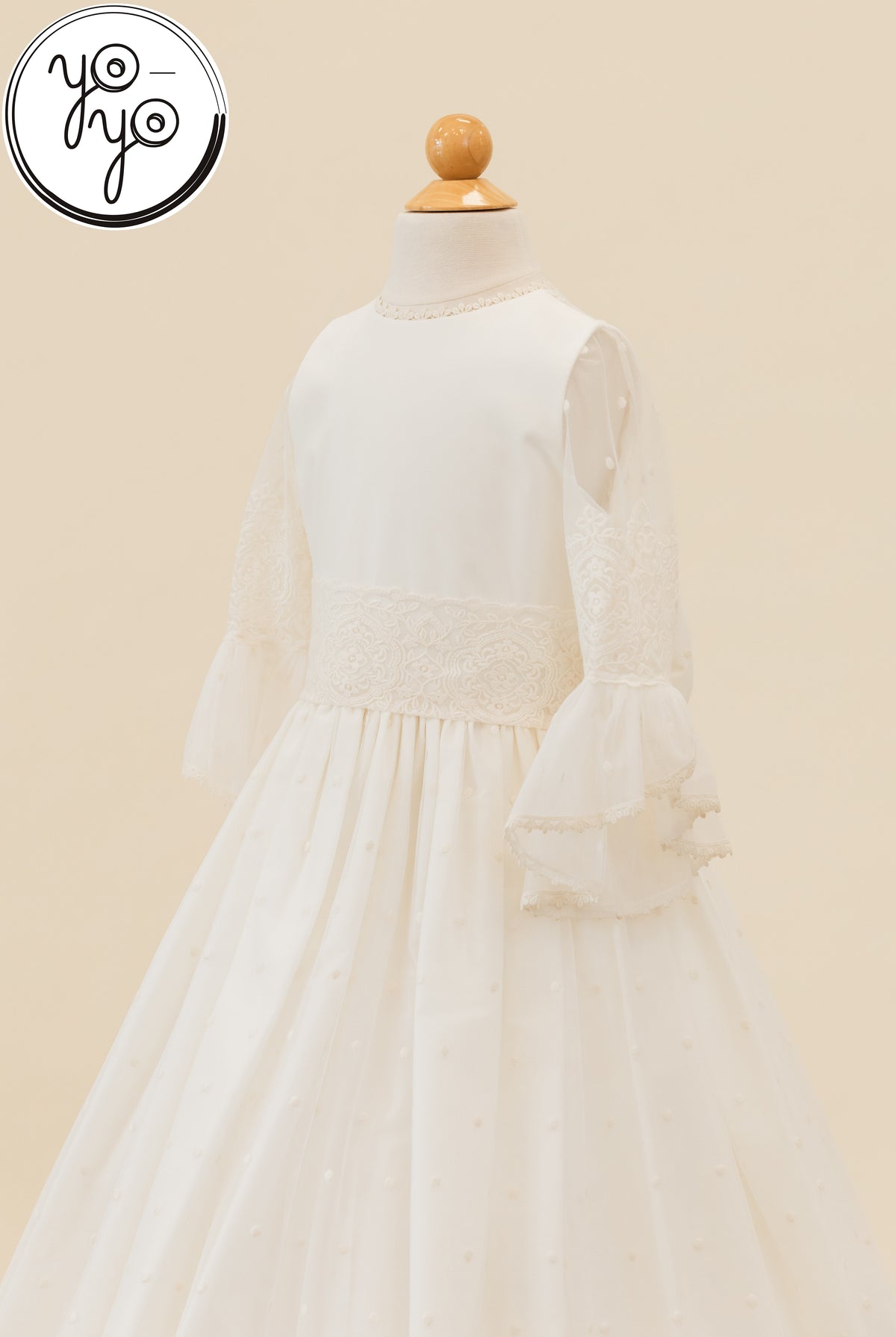 Manon Dress on a mannequin in off-white embroidered tulle with sheer ruffled sleeves, a lace waistband, and a dotted texture skirt.