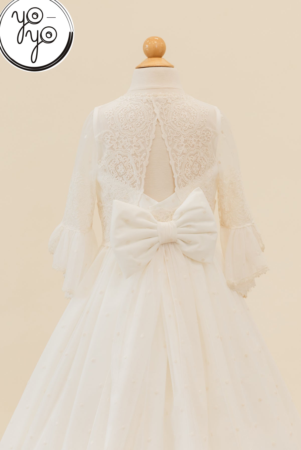 Back view of the white Manon Dress by YoYo Boutique, featuring embroidered tulle, a lace bodice, a cutout back, a large bow, and sheer sleeves.