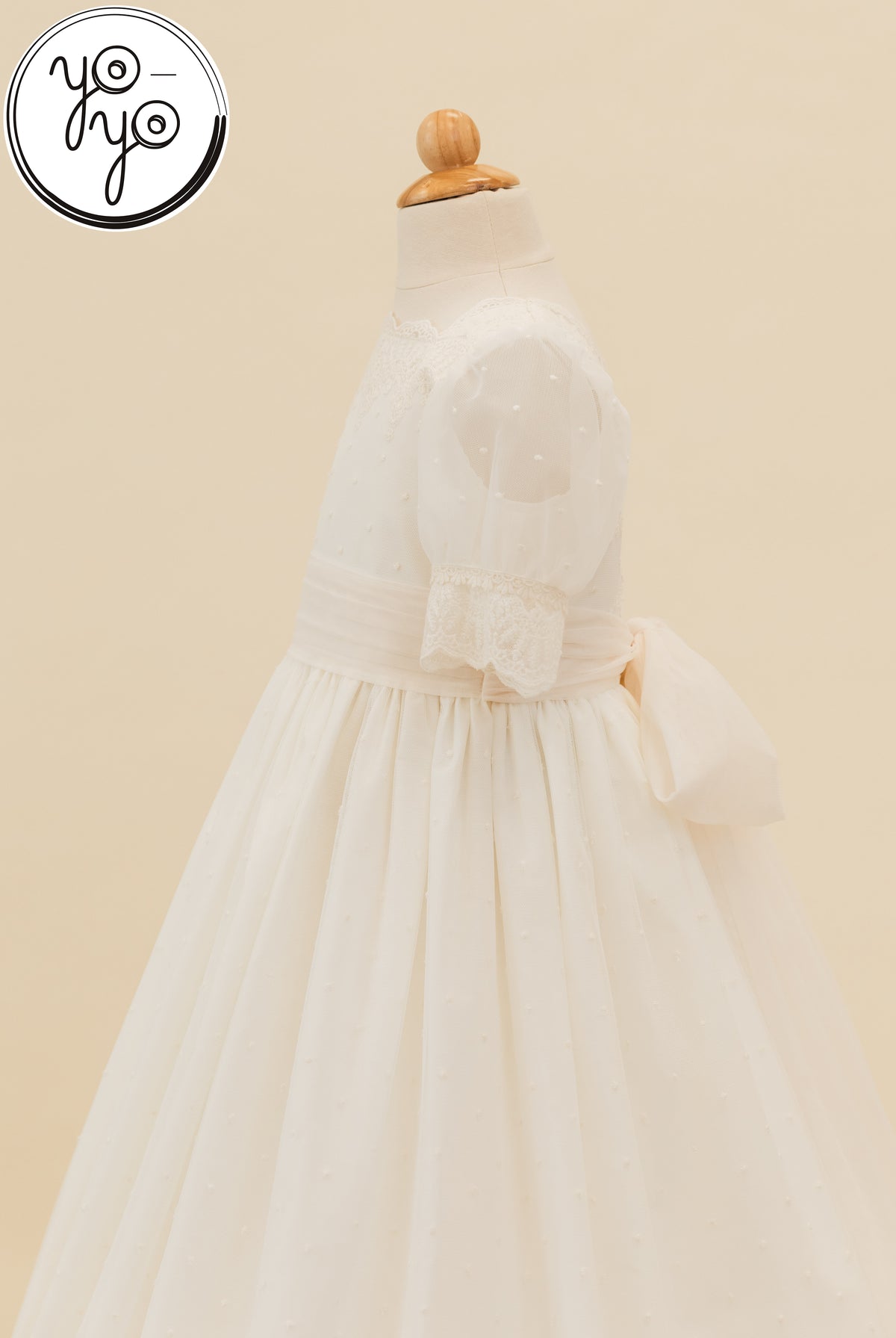 YoYo Boutique Sophie cream boho First Communion dress on a mannequin, featuring puffed sleeves, a lace bodice, and a large back bow.