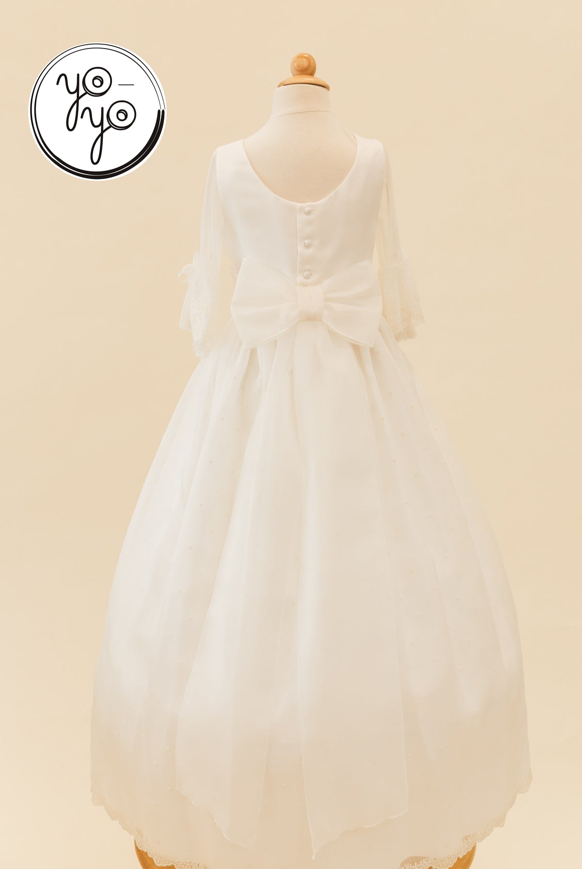 Back view of the white, floor-length Ceibo Dress by YoYo Boutique, featuring sheer French sleeves, a large back bow, and button closures.