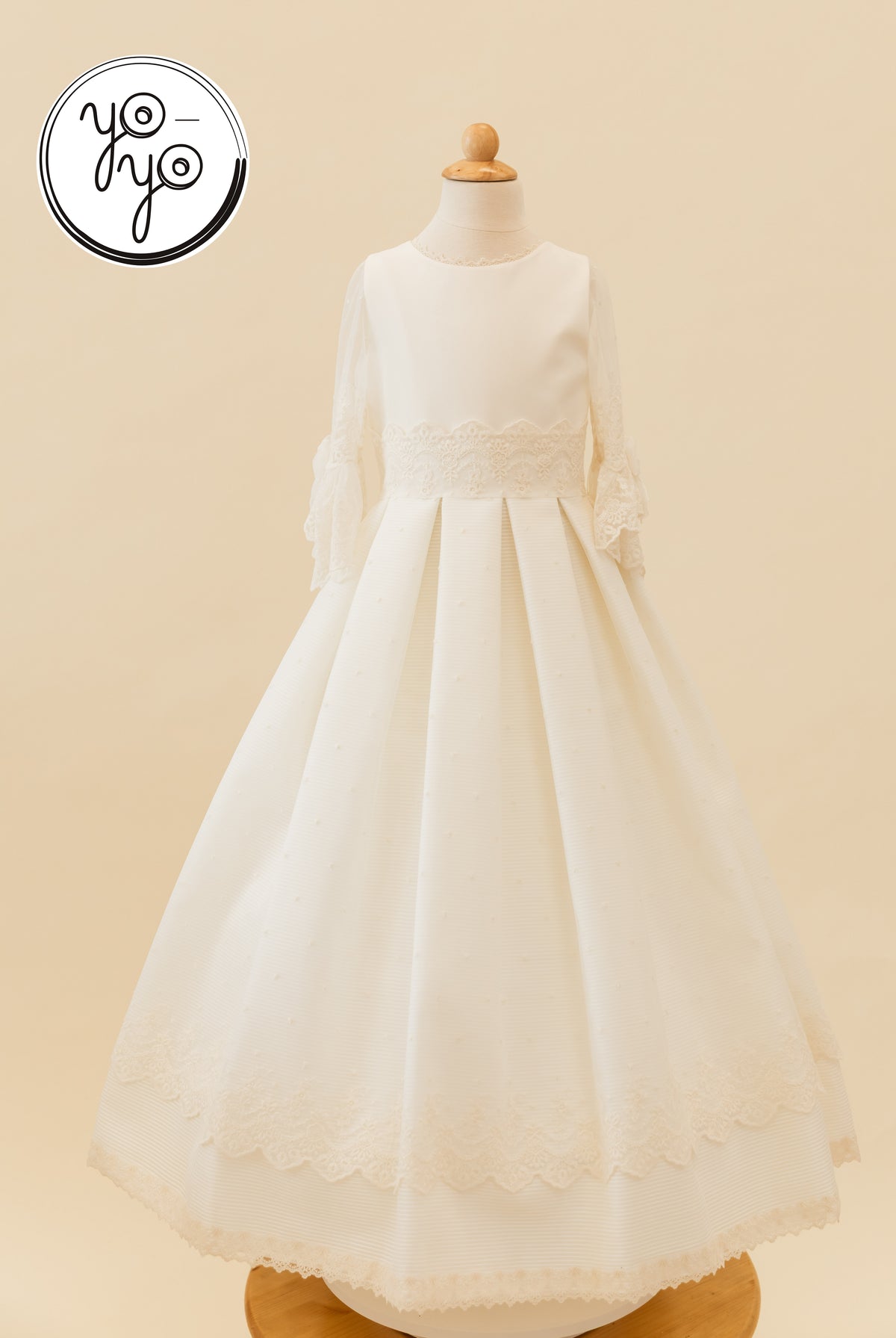 Giselle Deluxe First Communion dress in off-white, featuring a round neck, lace sleeves, and a lace-trimmed pleated floor-length skirt.