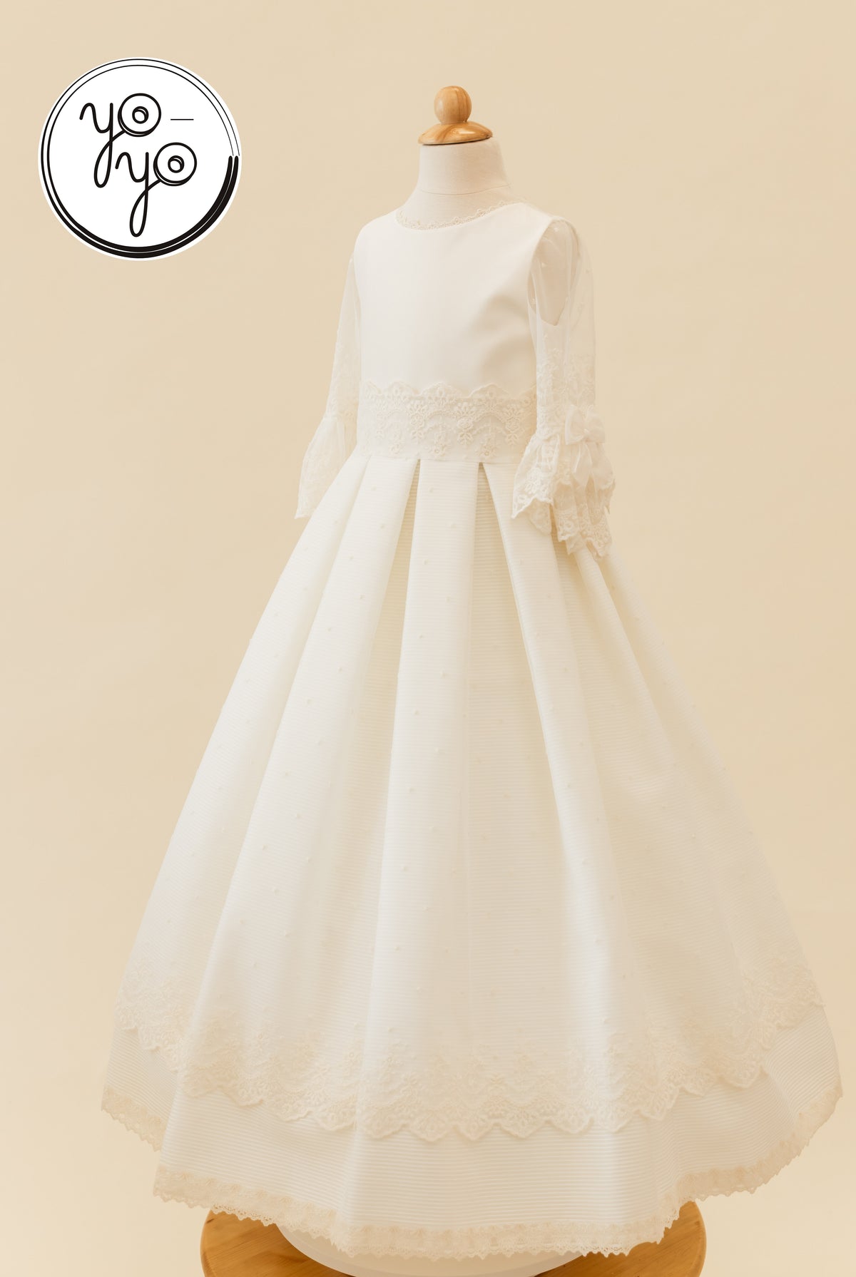 Giselle Deluxe dress in cream, featuring lace-trimmed sleeves, a cinched waist, and a floor-length pleated skirt with a lace hem.
