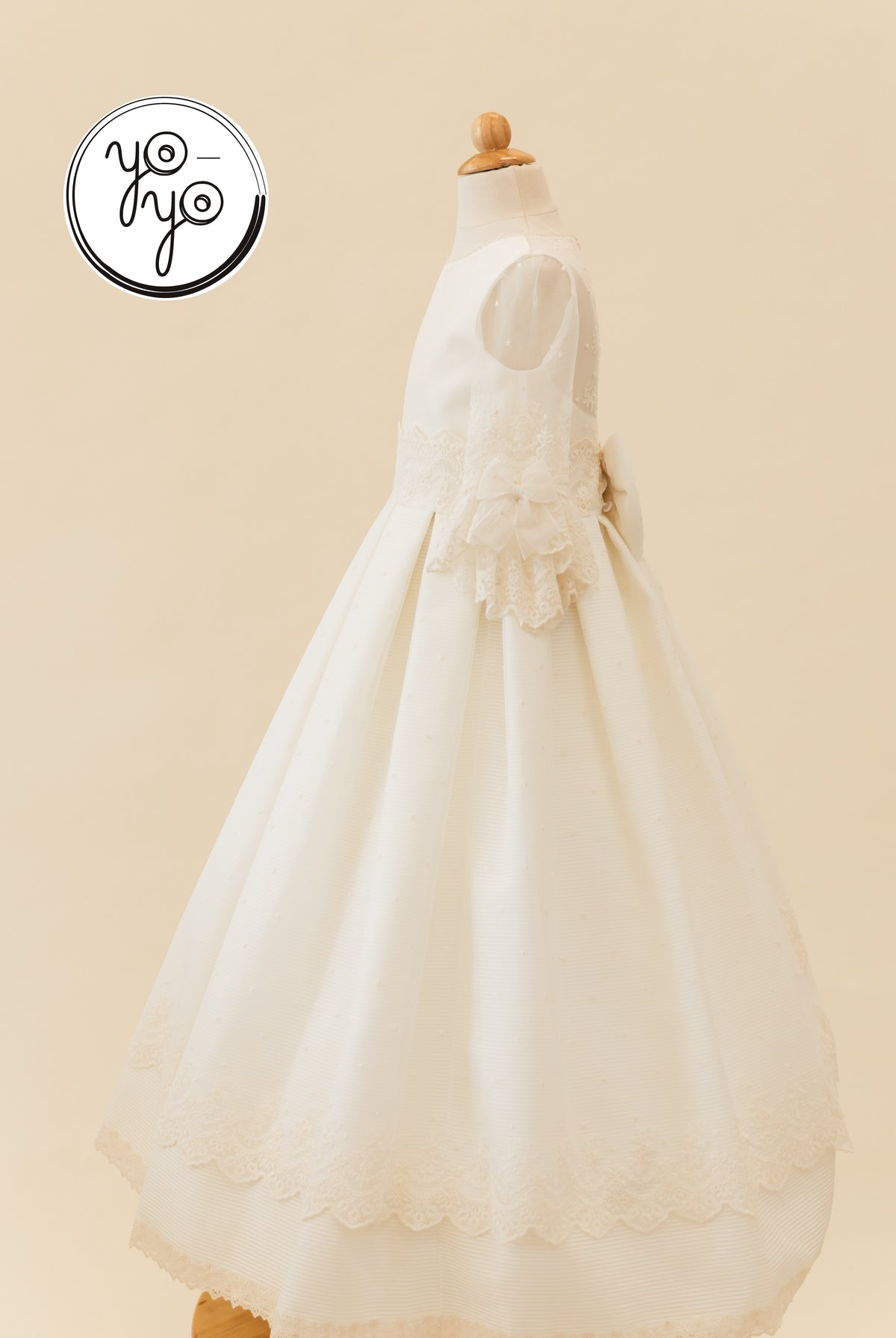 Side view of the white embroidered tulle Giselle Deluxe Dress, featuring sheer sleeves, lace cuffs, and a large back waist bow.