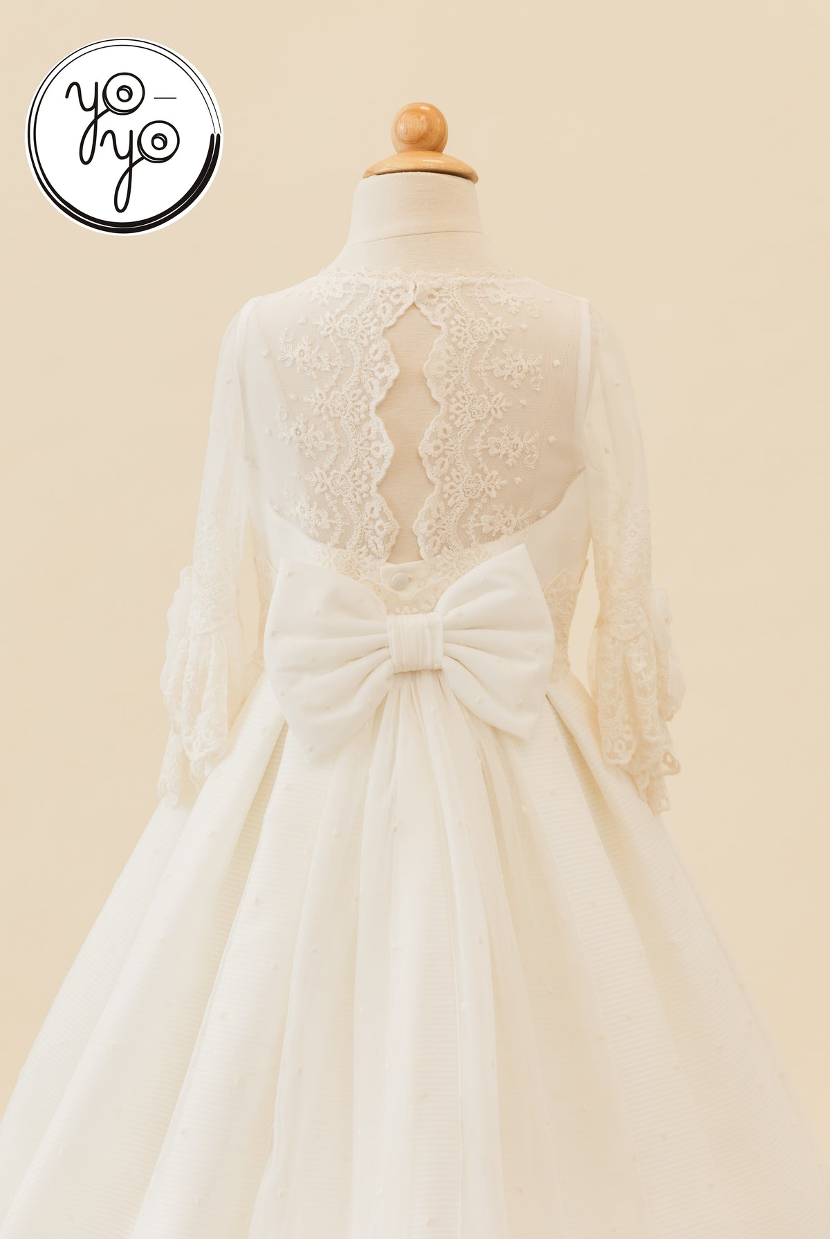 Back view of the cream Giselle Deluxe Dress, featuring a lace bodice, long sleeves, and a large waist bow.