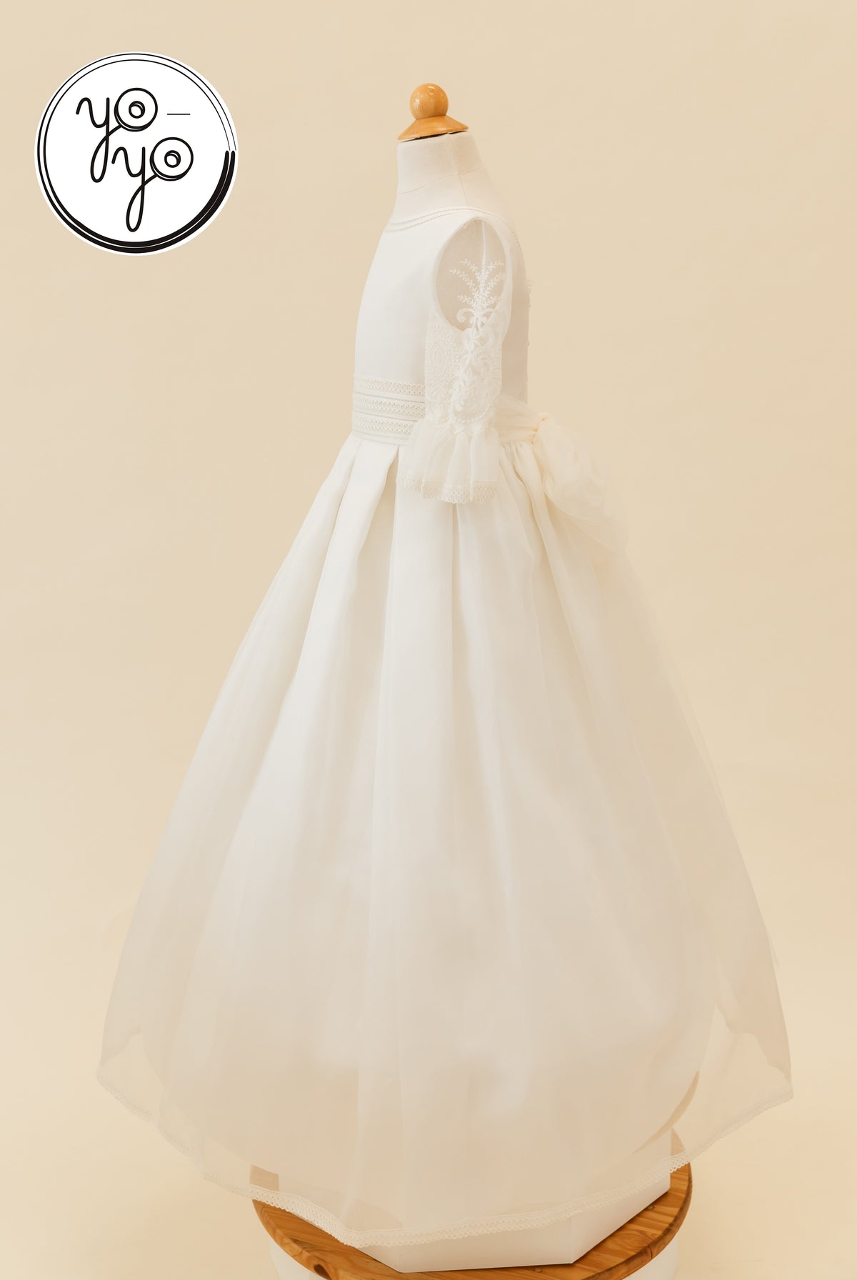 The Magnolia Dress by YoYo Boutique: a rustic gauze First Communion dress on a mannequin featuring lace sleeves, a high waist, and a back bow.