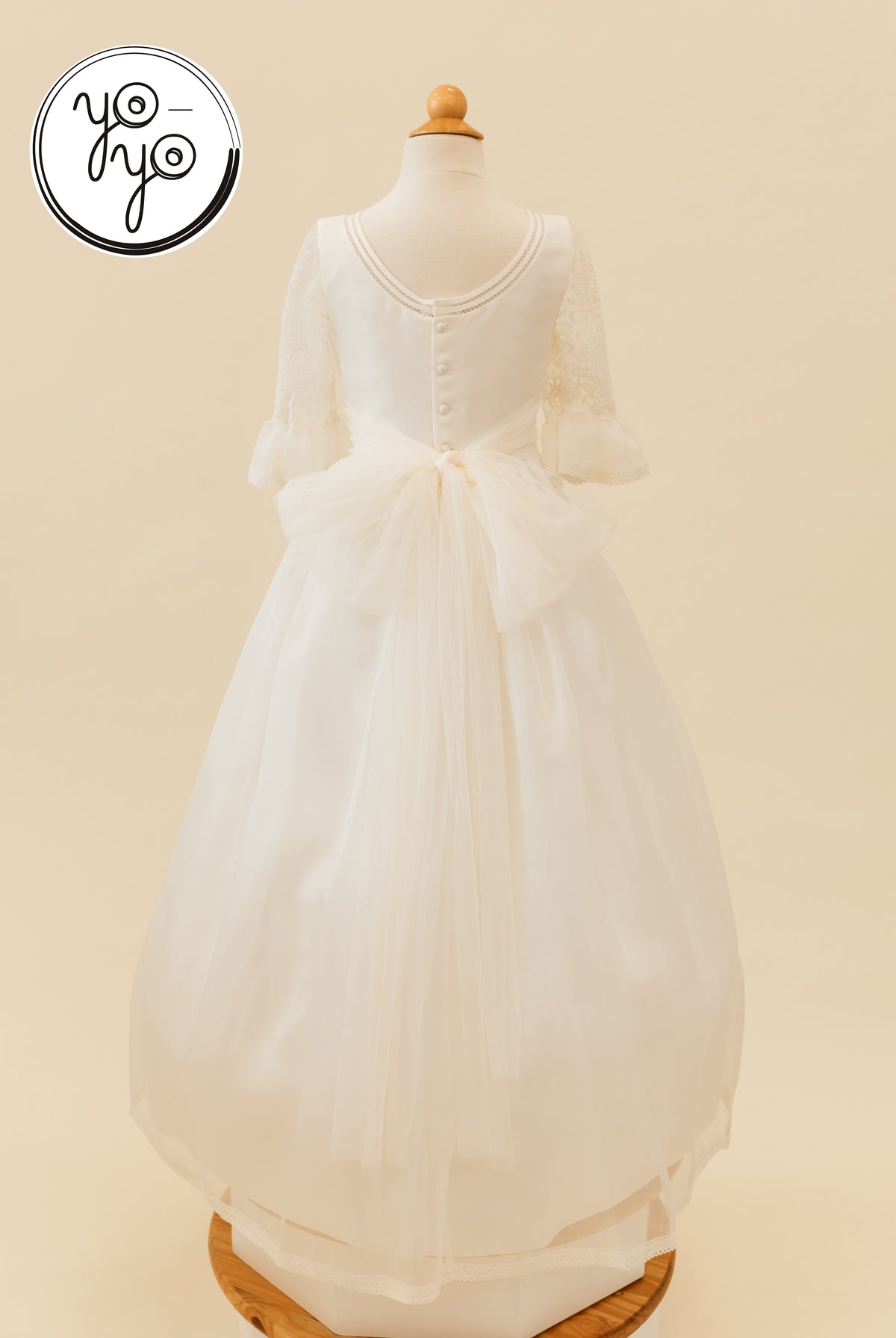 Back view of the white Magnolia Dress featuring embroidered lace, three-quarter sleeves, a scoop back with button closures, and a large tulle bow.