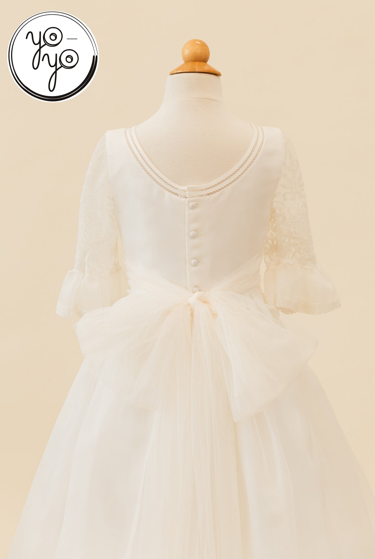Back view of the off-white Magnolia Dress by YoYo Boutique with elbow-length lace sleeves, a buttoned bodice, and a tulle bow.