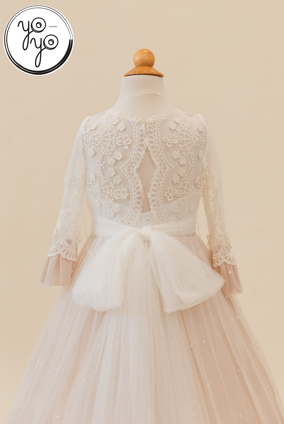 Back view of the cream Lua Dress by YoYo Boutique, featuring long lace sleeves, a cutout back, and a large tulle bow at the waist.