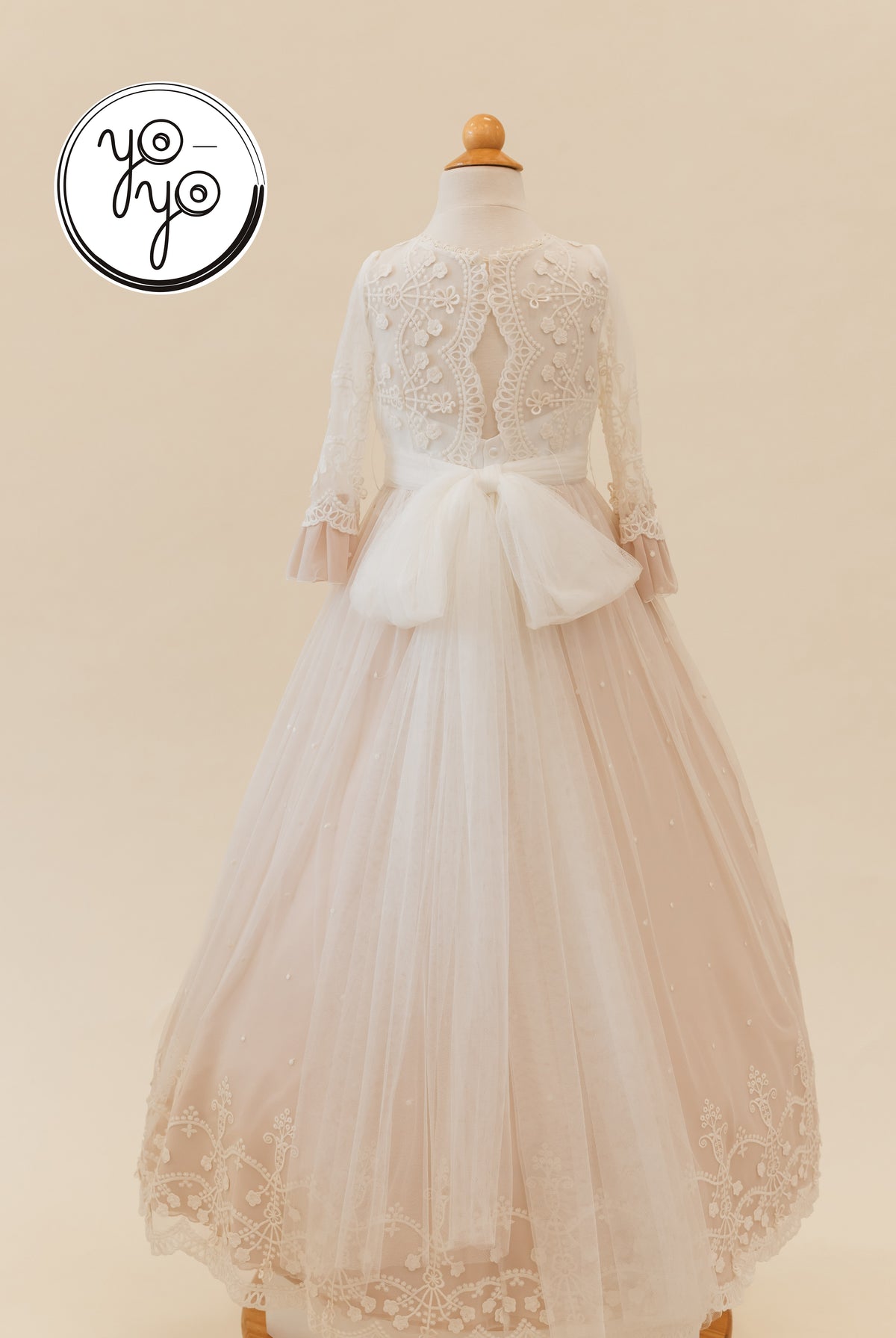 Back view of the cream Lua Dress by YoYo Boutique, featuring long lace sleeves, a waist bow, and an embroidered, full-length tulle skirt.