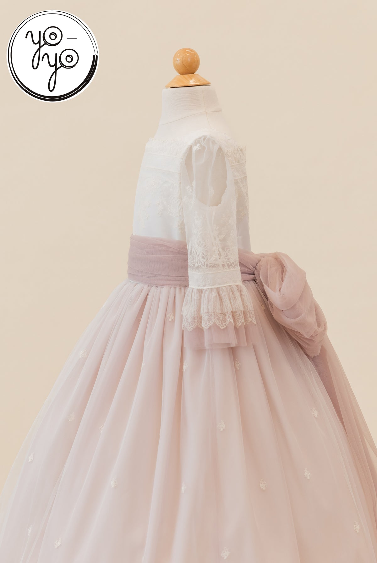 Elena Dress: A white boho Communion gown with lace sleeves and a dusty rose embroidered tulle skirt, finished with a large sash at the back.