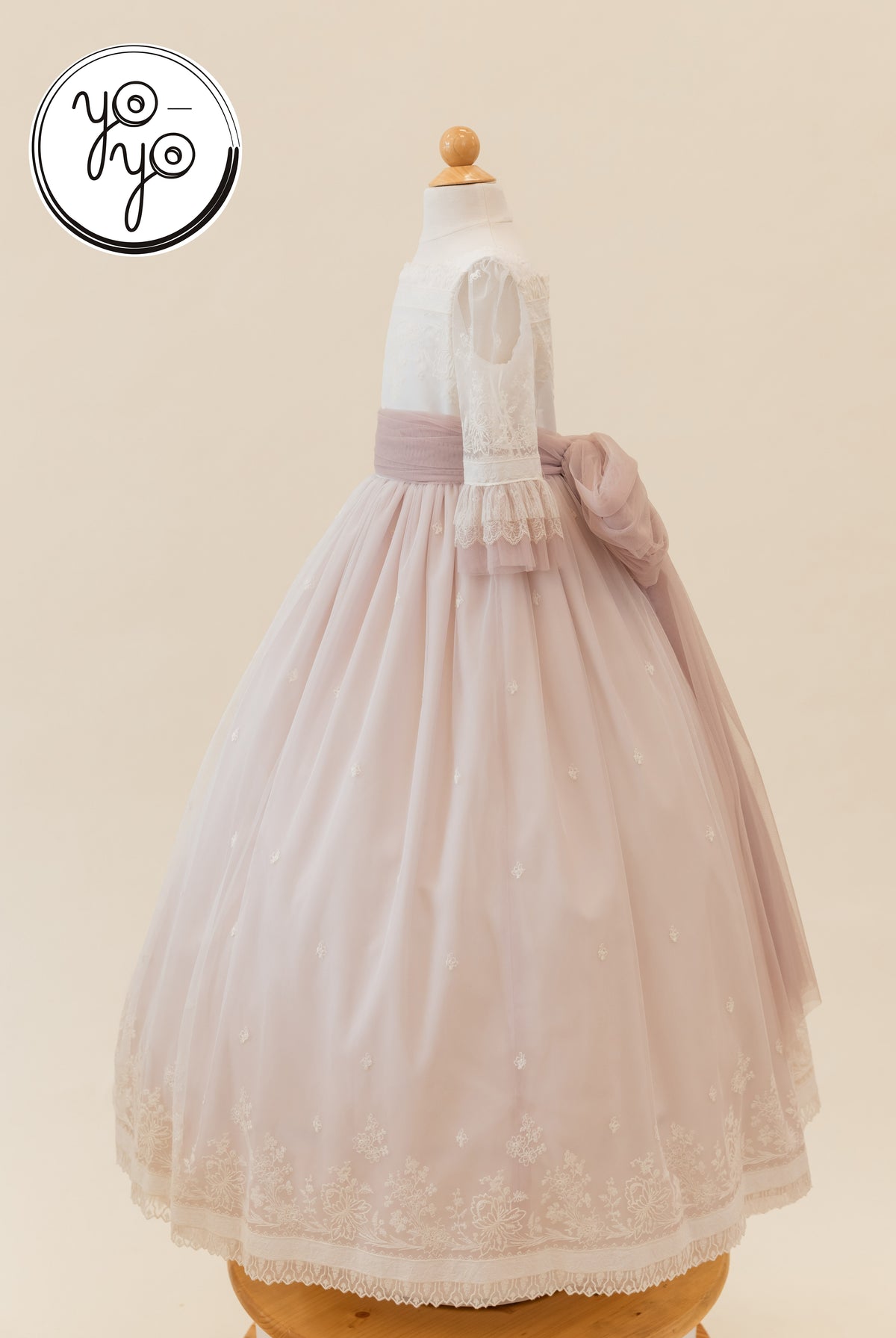The Elena Dress by YoYo Boutique features a white lace-trimmed bodice, a dusty pink embroidered French tulle skirt, and a large waist bow.