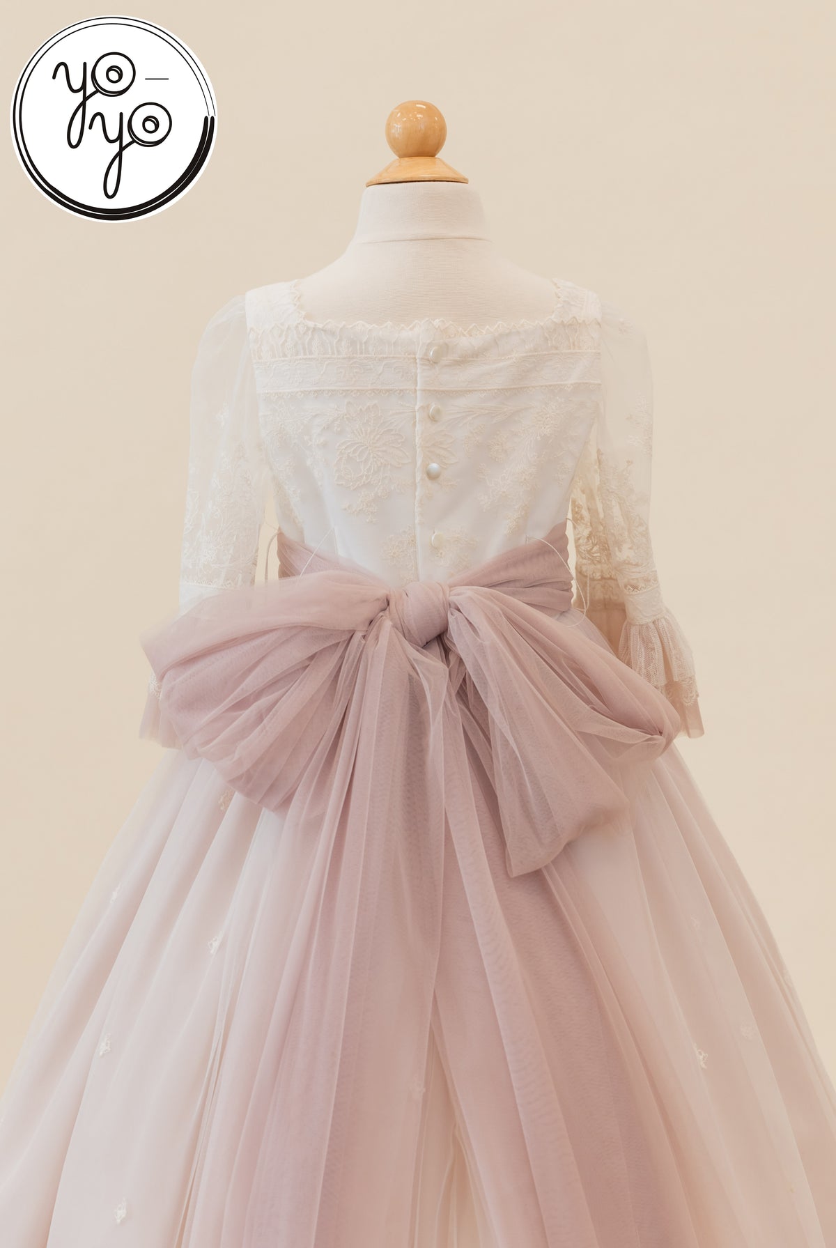 Back view of the white boho Elena Dress, featuring sheer three-quarter sleeves, button closures, and a large dusty rose tulle bow at the waist.
