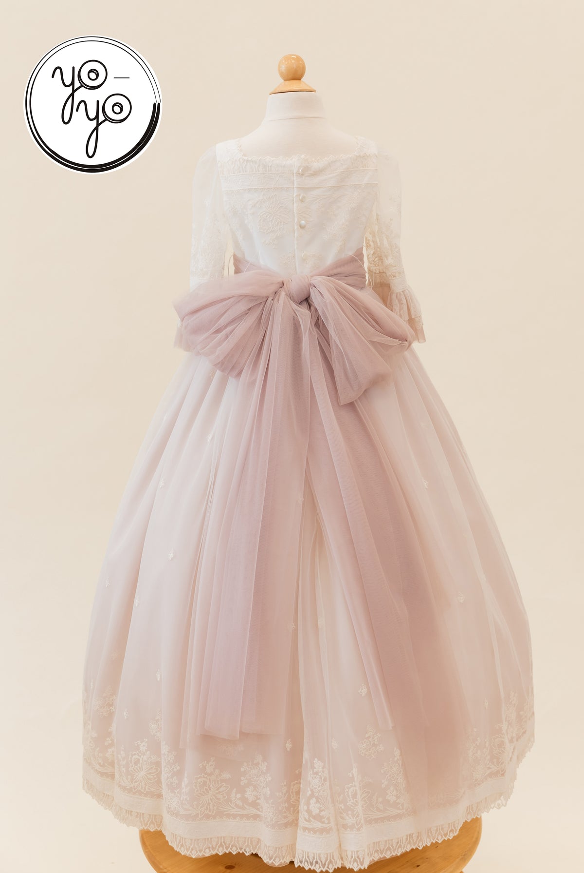 Back view of the Elena Dress by YoYo Boutique: a white lace boho Communion gown with long sleeves and a large, dusty pink tulle waist bow.