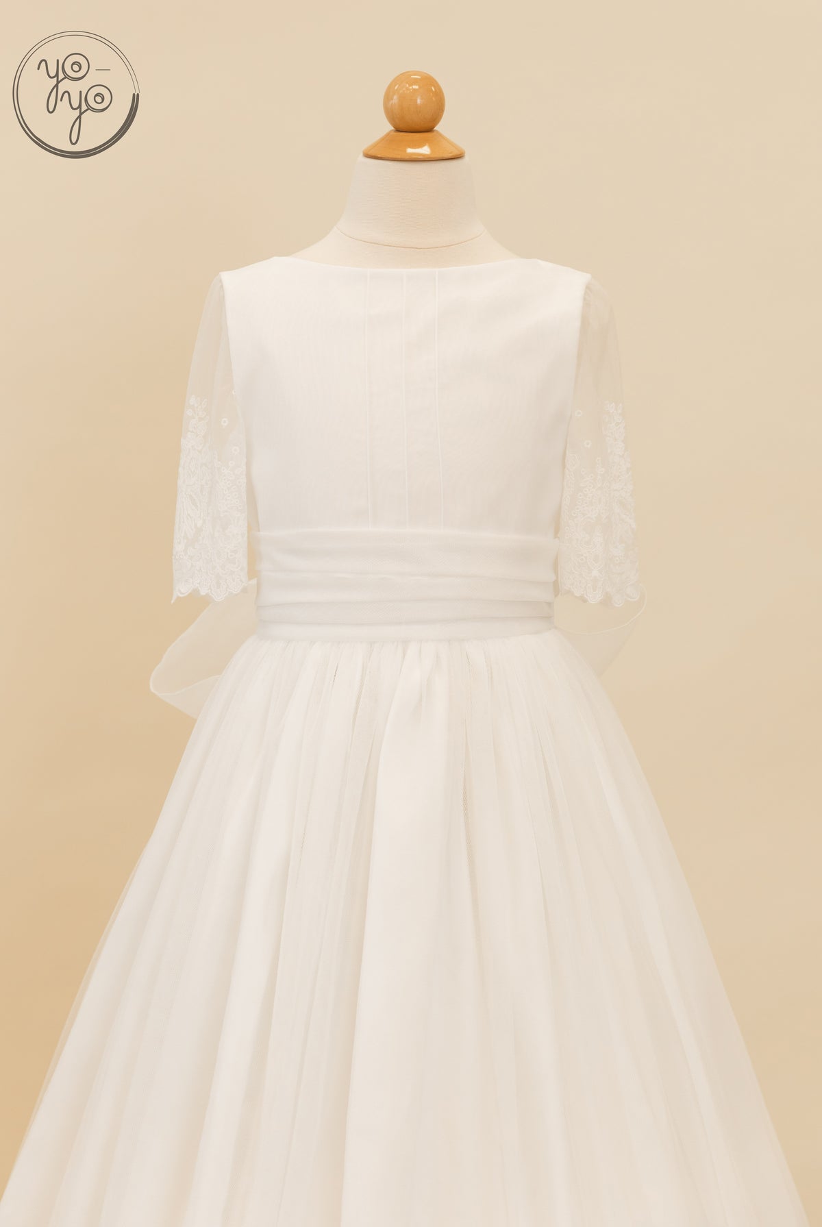 White Nigella dress on a mannequin with a boat neckline, sheer lace sleeves, a pleated waistband, and a full French tulle skirt.