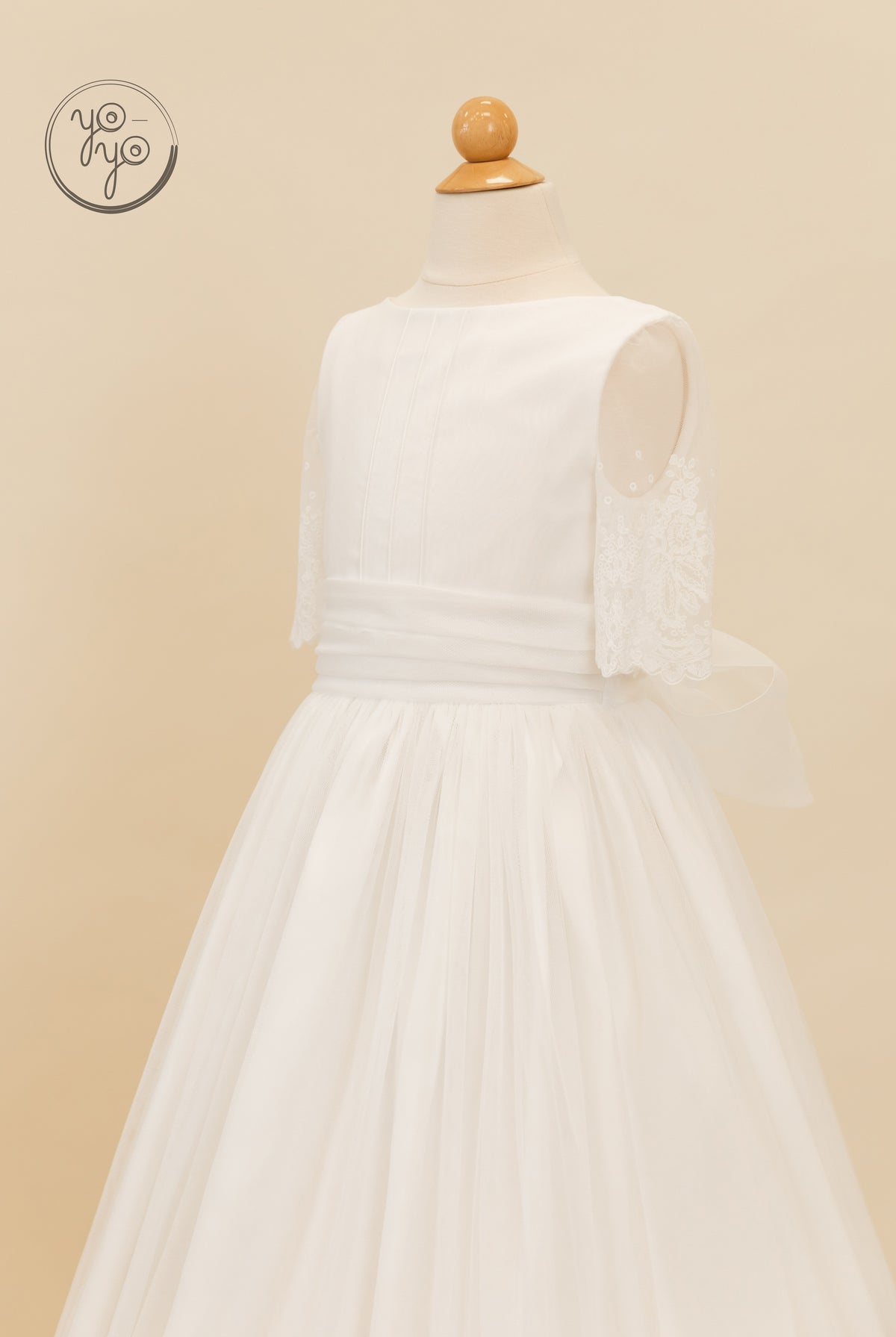 Nigella Dress: A white sleeveless First Communion dress featuring a scoop neck, pleated bodice, lace accents, and a boho tulle skirt with a bow.