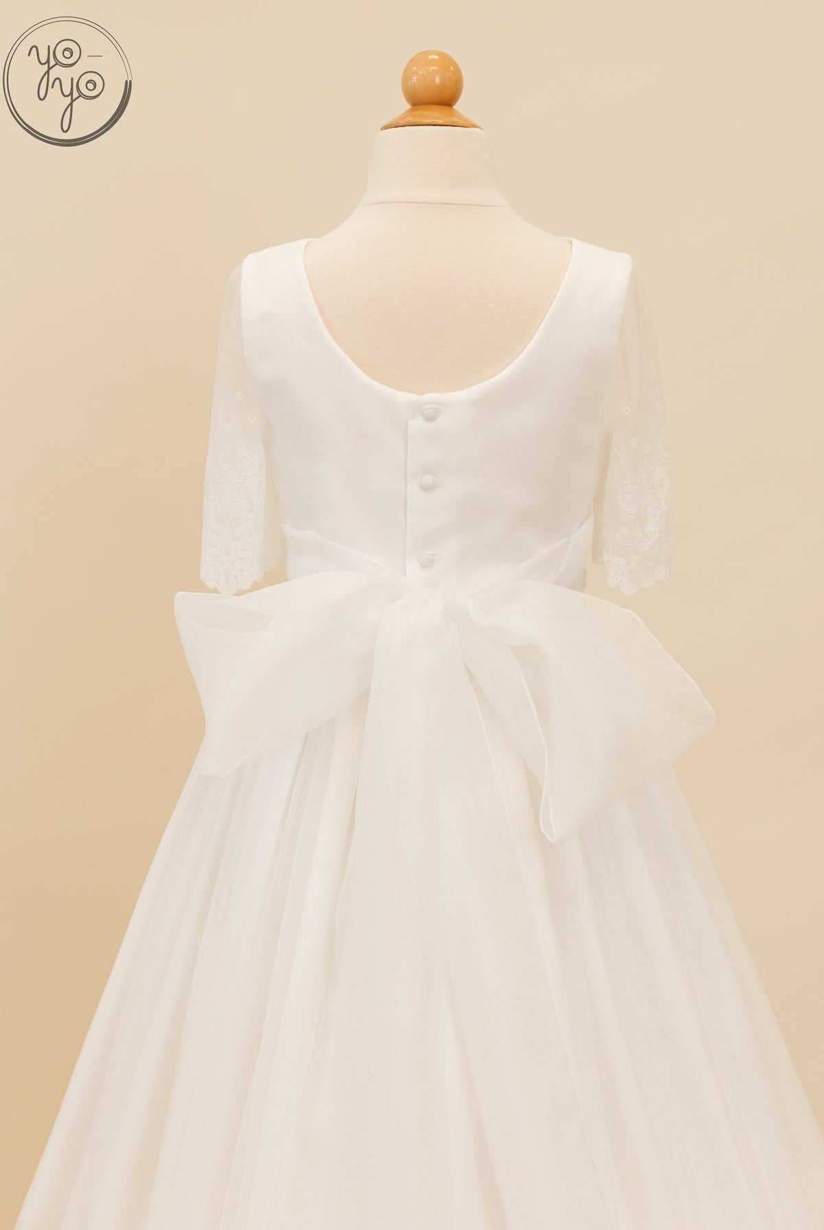 Back view of the white Nigella Dress by YoYo Boutique, featuring lace elbow-length sleeves, a button-back bodice, and a large sheer waist bow.