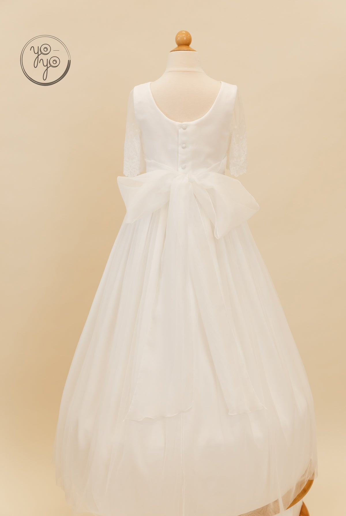 Back view of the Nigella Dress: a floor-length, boho-style gown featuring a scooped back, button closures, and a large sheer waist bow.