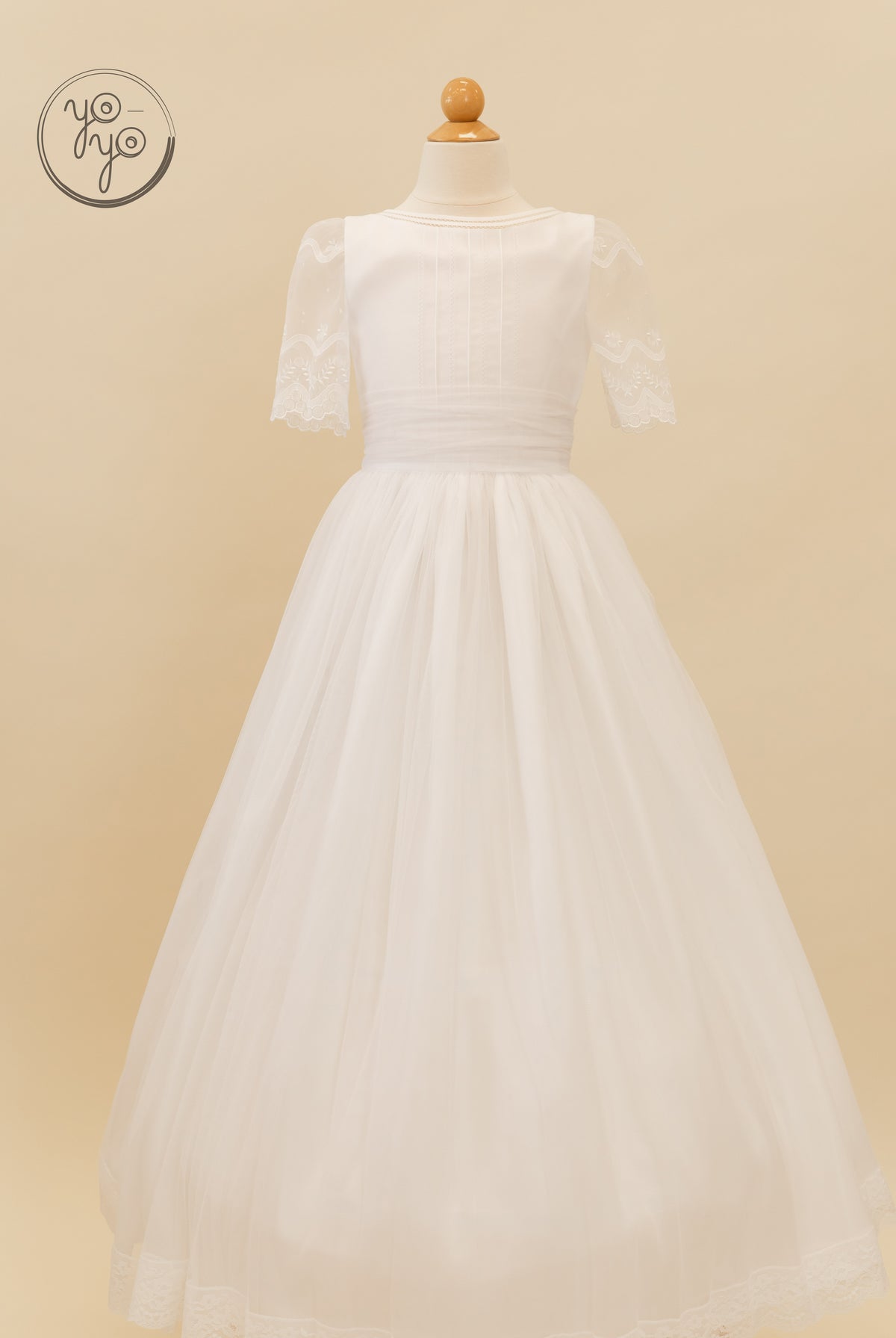 The white Lunaria A-line First Communion dress features a high neckline, short lace sleeves, and a sheer boho tulle skirt.