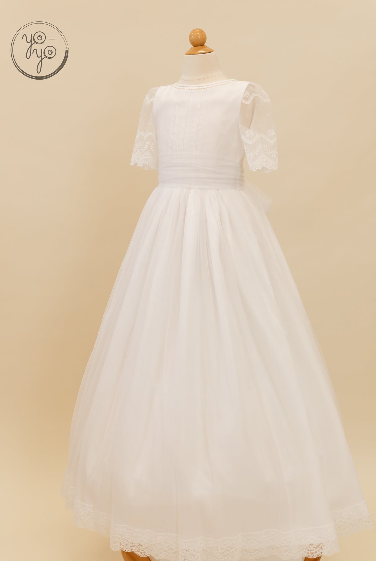 The white Lunaria Dress by YoYo Boutique features sheer lace sleeves, a cinched waist, and a floor-length tulle skirt.