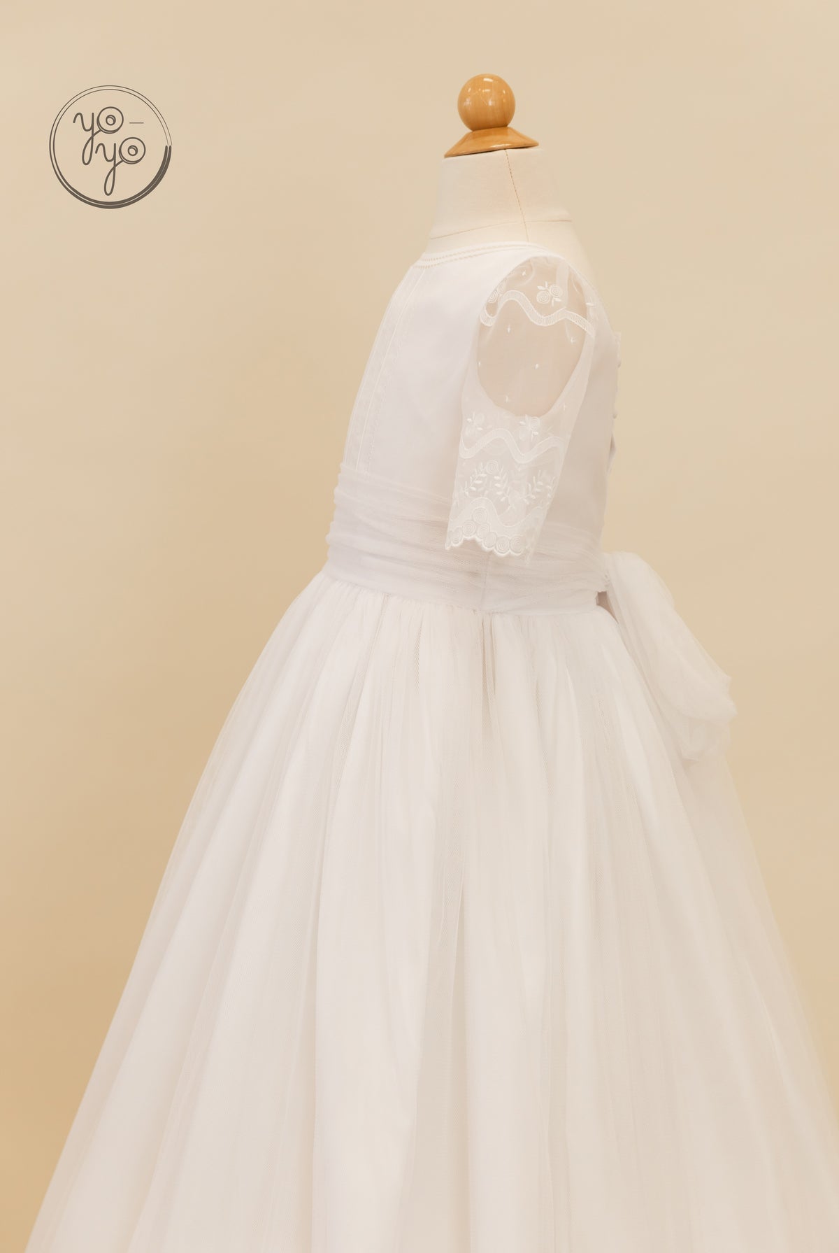 Side view of the white organza Lunaria Dress by YoYo Boutique on a mannequin, showing sheer embroidered elbow-length sleeves and a tulle skirt.