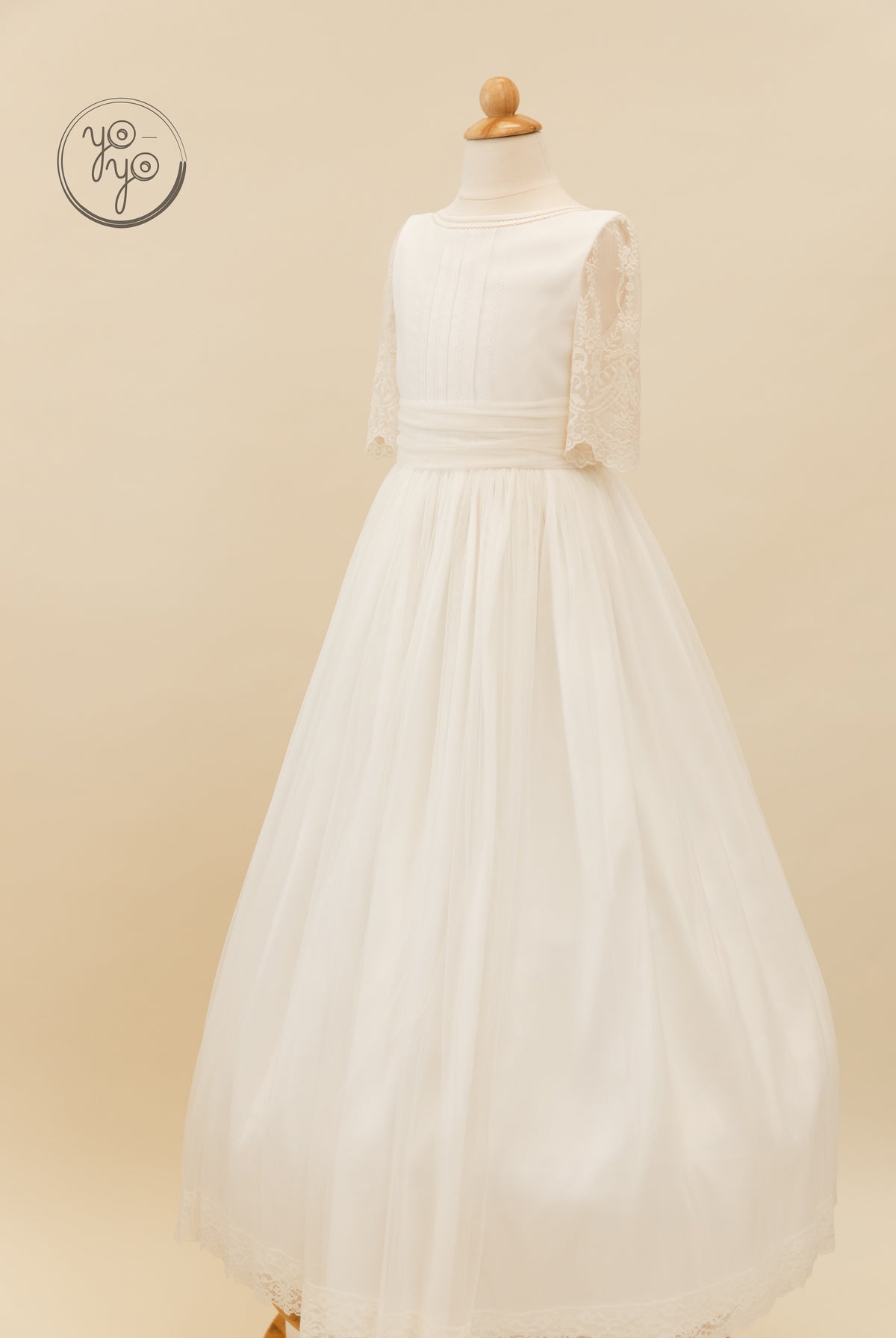 Off-white floor-length Melisa Dress on a form, featuring a round neckline, pleated bodice, and elbow-length lace tulle sleeves.