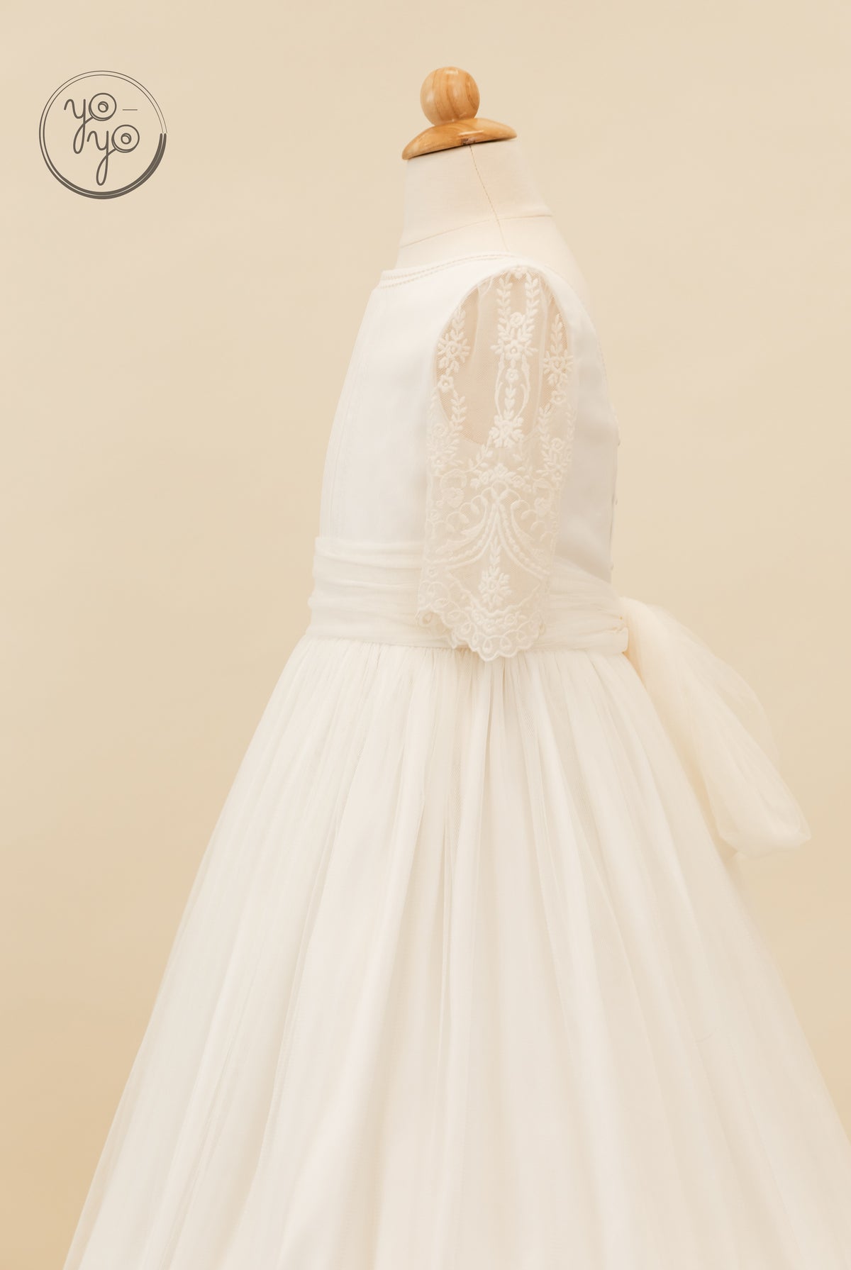 Side view of the white lace Melisa Dress featuring three-quarter sleeves, a wide waistband, and a tulle skirt with a large back bow.