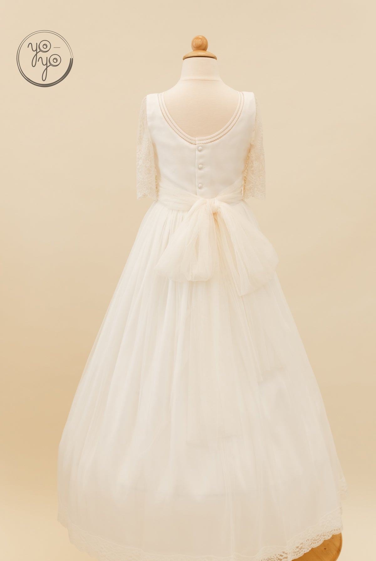 Back view of the white lace tulle Melisa dress featuring a scooped back, a row of buttons, and a large waist bow.