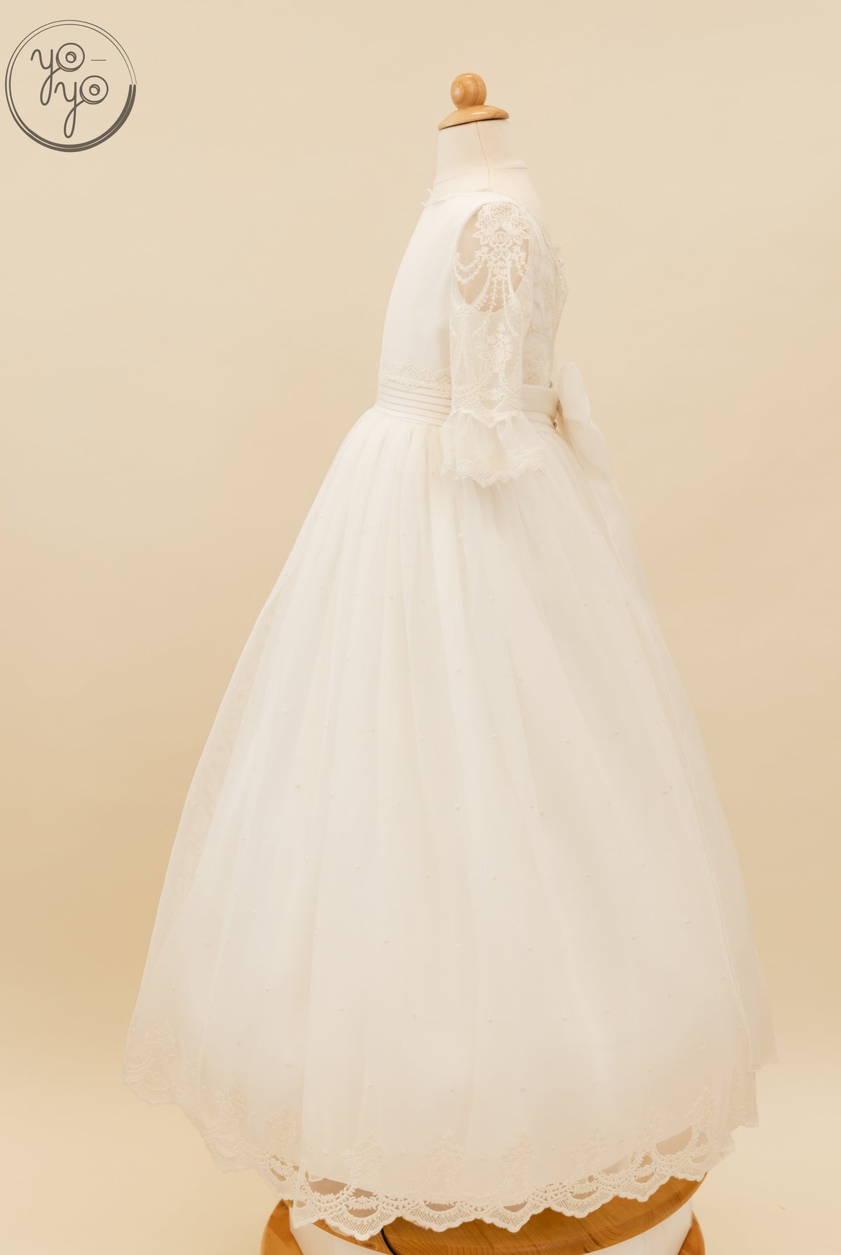 Side view of the Nerina Dress by YoYo Boutique, featuring sheer lace sleeves, a pleated waist with a bow, and a full skirt with pearl accents.