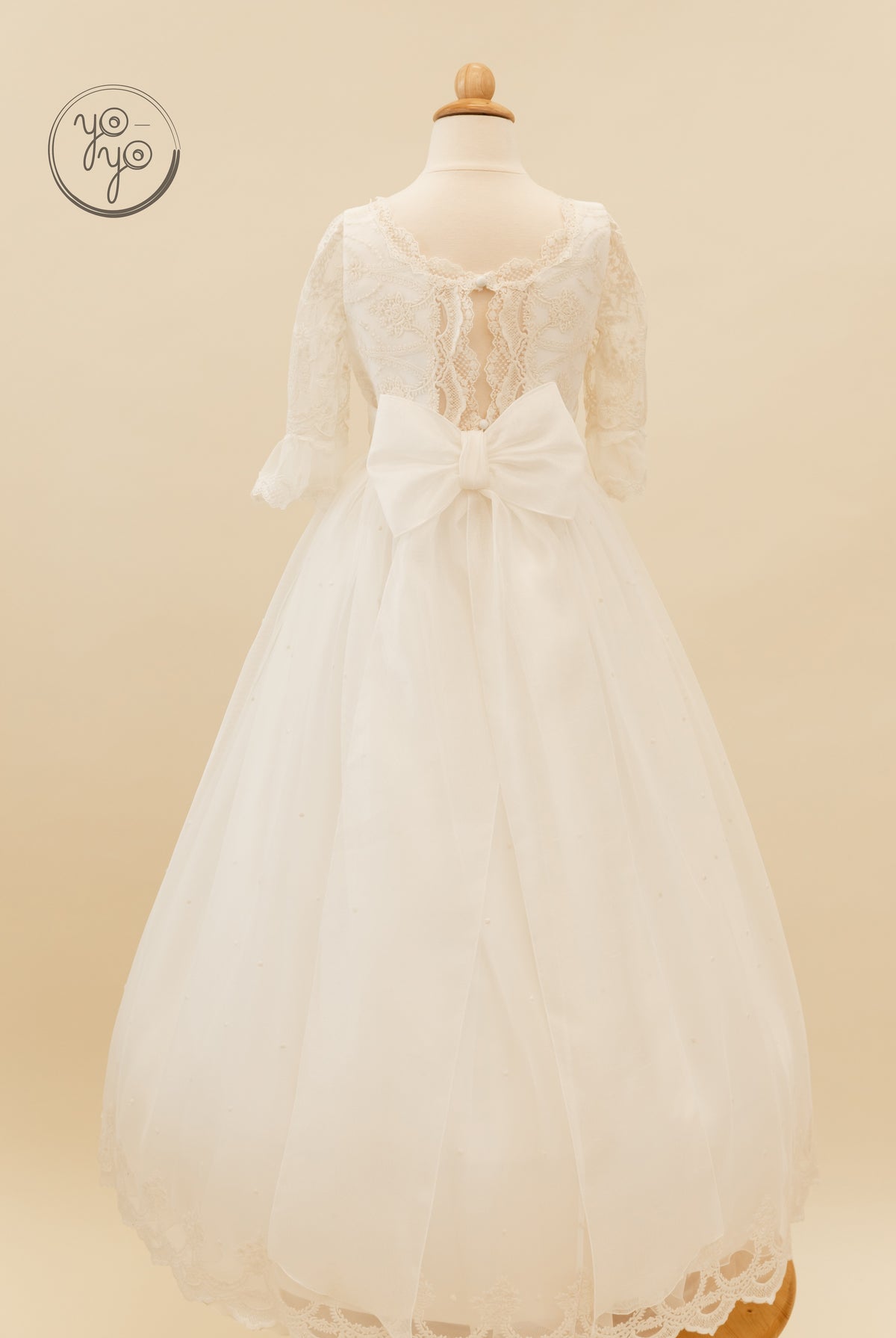 Back view of a Nerina Dress by YoYo Boutique, featuring a boho lace bodice with a back cutout, large waist bow, and pearl-accented French tulle skirt.