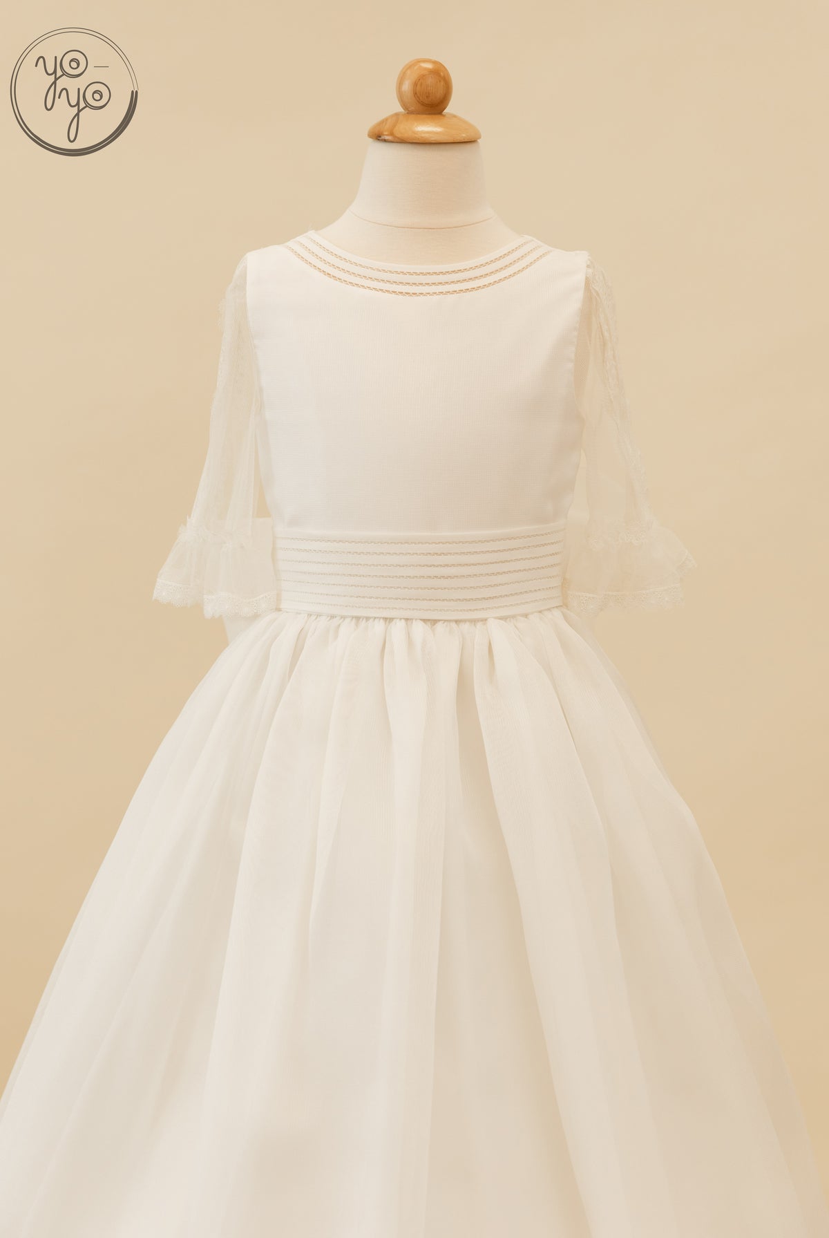 Jacinto Dress by YoYo Boutique: white boho First Communion dress on a mannequin with sheer 3/4 sleeves, a braided neckline, and a wide waist.
