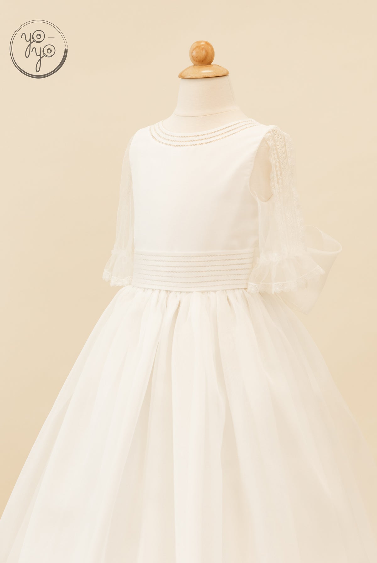 Jacinto Dress by YoYo Boutique: white boho Communion dress on a mannequin featuring a beaded neckline, sheer lace sleeves, and a pleated skirt.