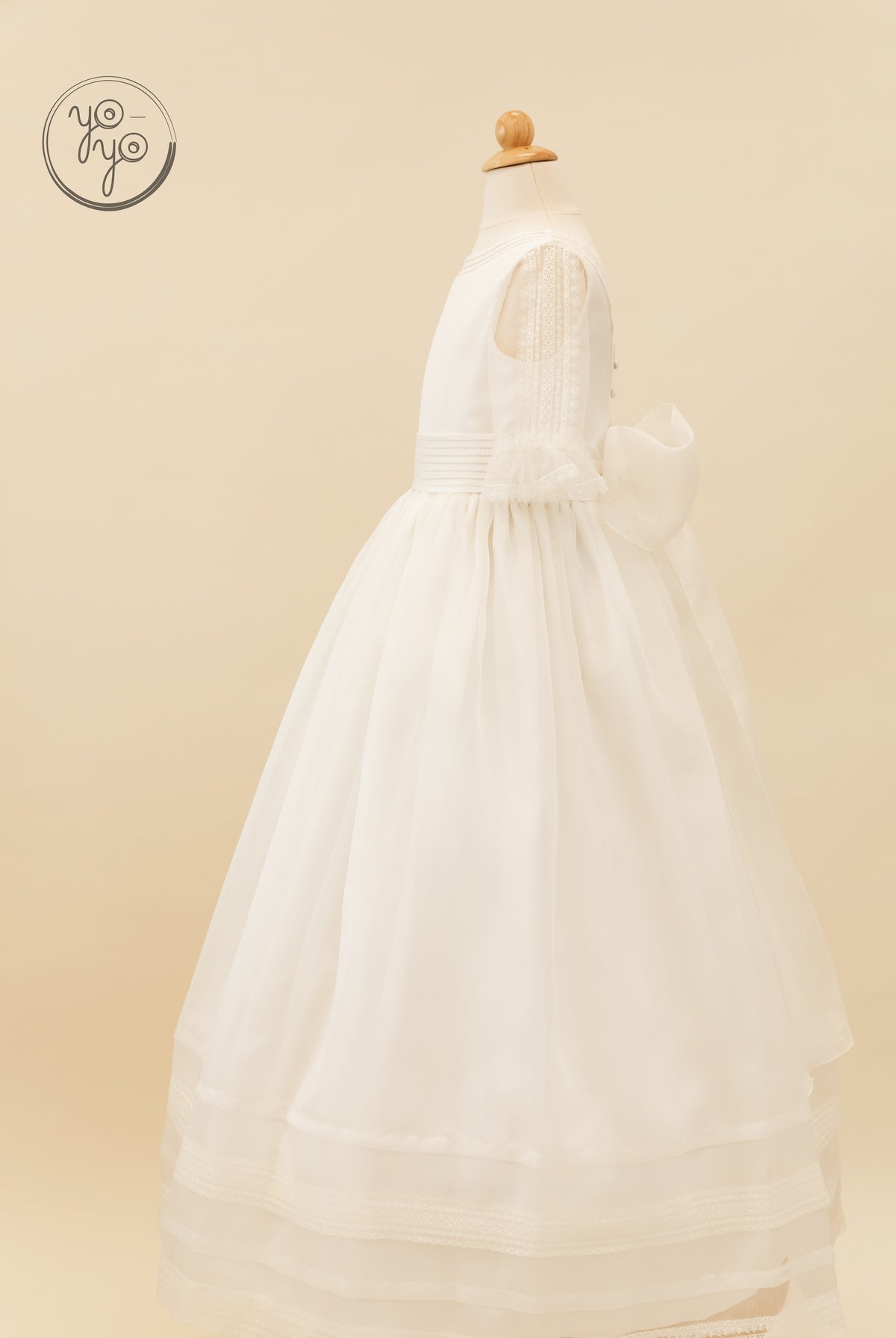 Side view of a white rustic gauze Jacinto Dress by YoYo Boutique featuring a full skirt, ruffled sleeves, and a large back waist bow.