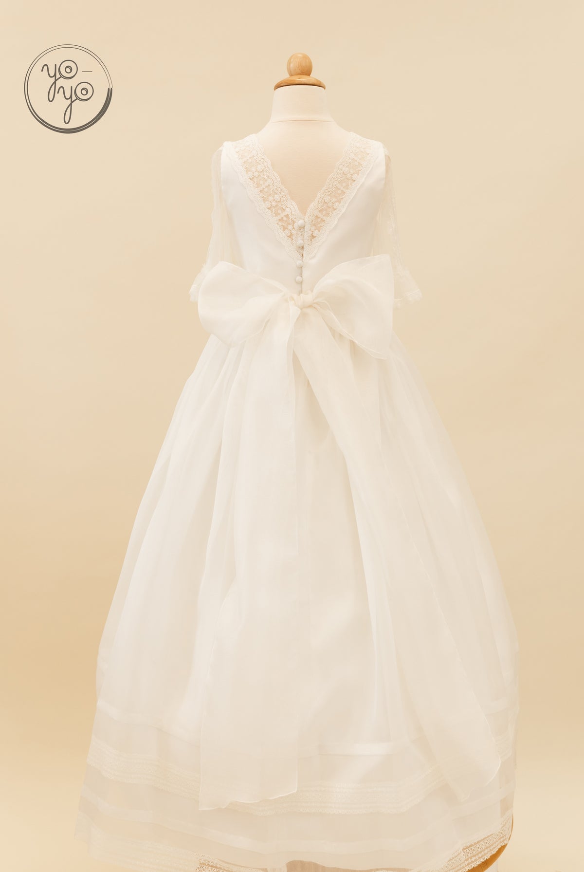 Back view of the white Jacinto dress by YoYo Boutique, featuring a lace bodice, a large sheer waist bow, and a lace-trimmed full skirt.