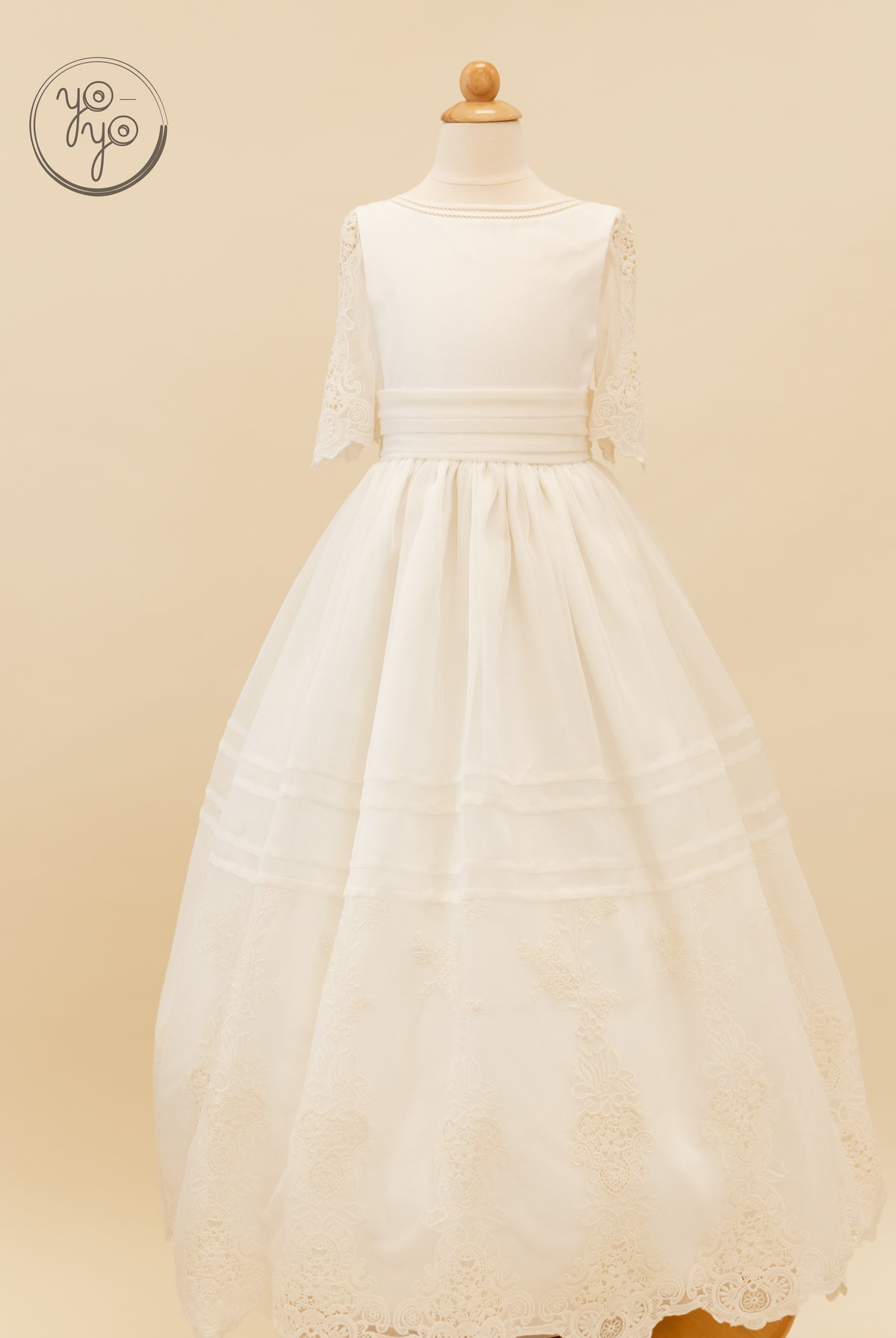 Ivory Coral dress featuring elbow-length lace sleeves, a pleated waistband, and a full skirt with a floral lace border.