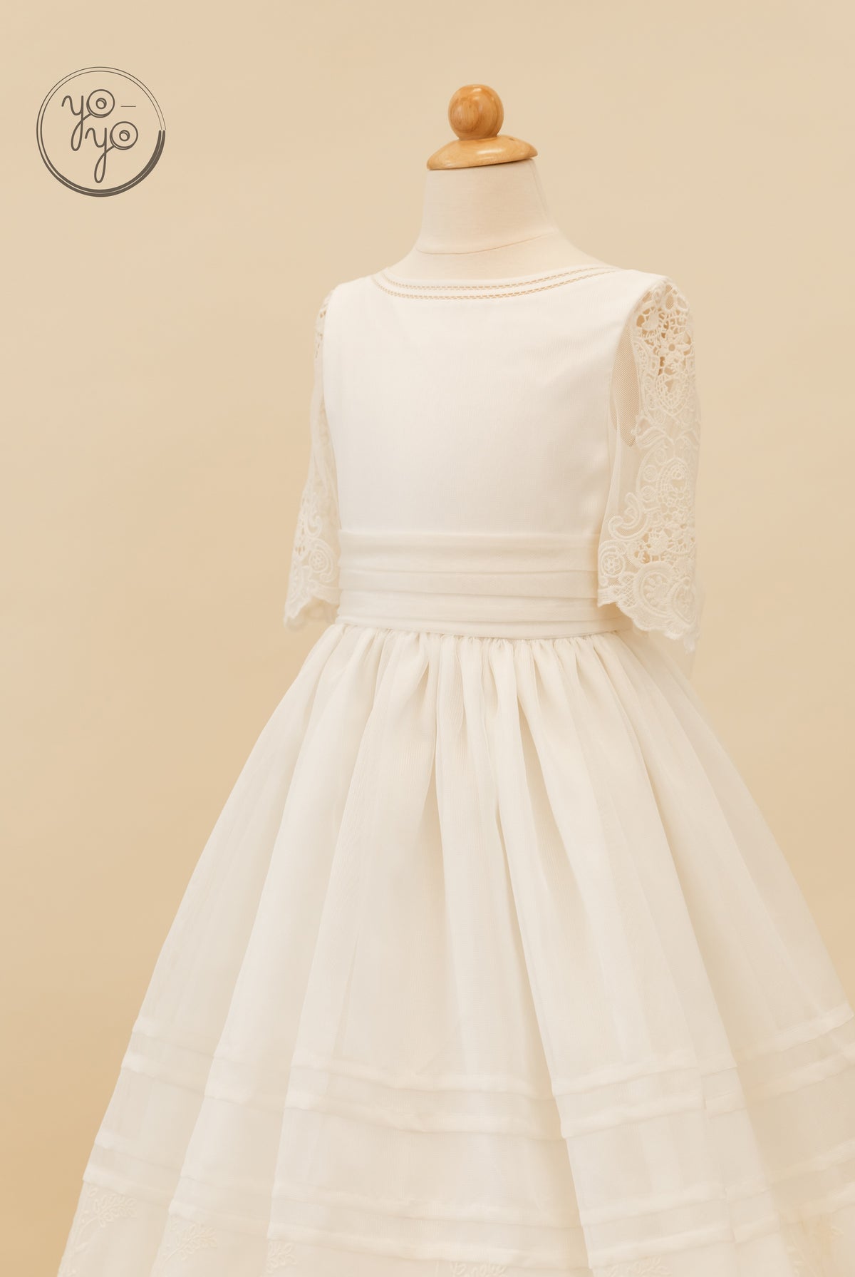 Off-white boho Coral First Communion dress with a pleated waist, boat neckline, and sheer lace sleeves.