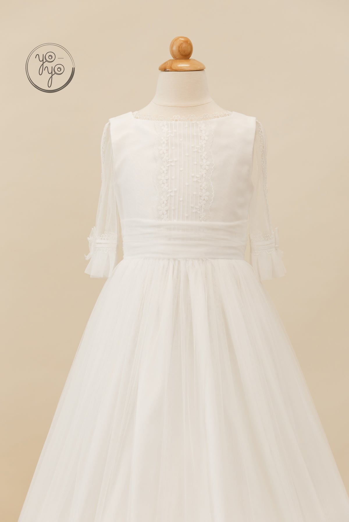 Valeriana Dress by YoYo Boutique: a white boho communion dress with a lace-trimmed neckline, sheer three-quarter sleeves, and a full tulle skirt.