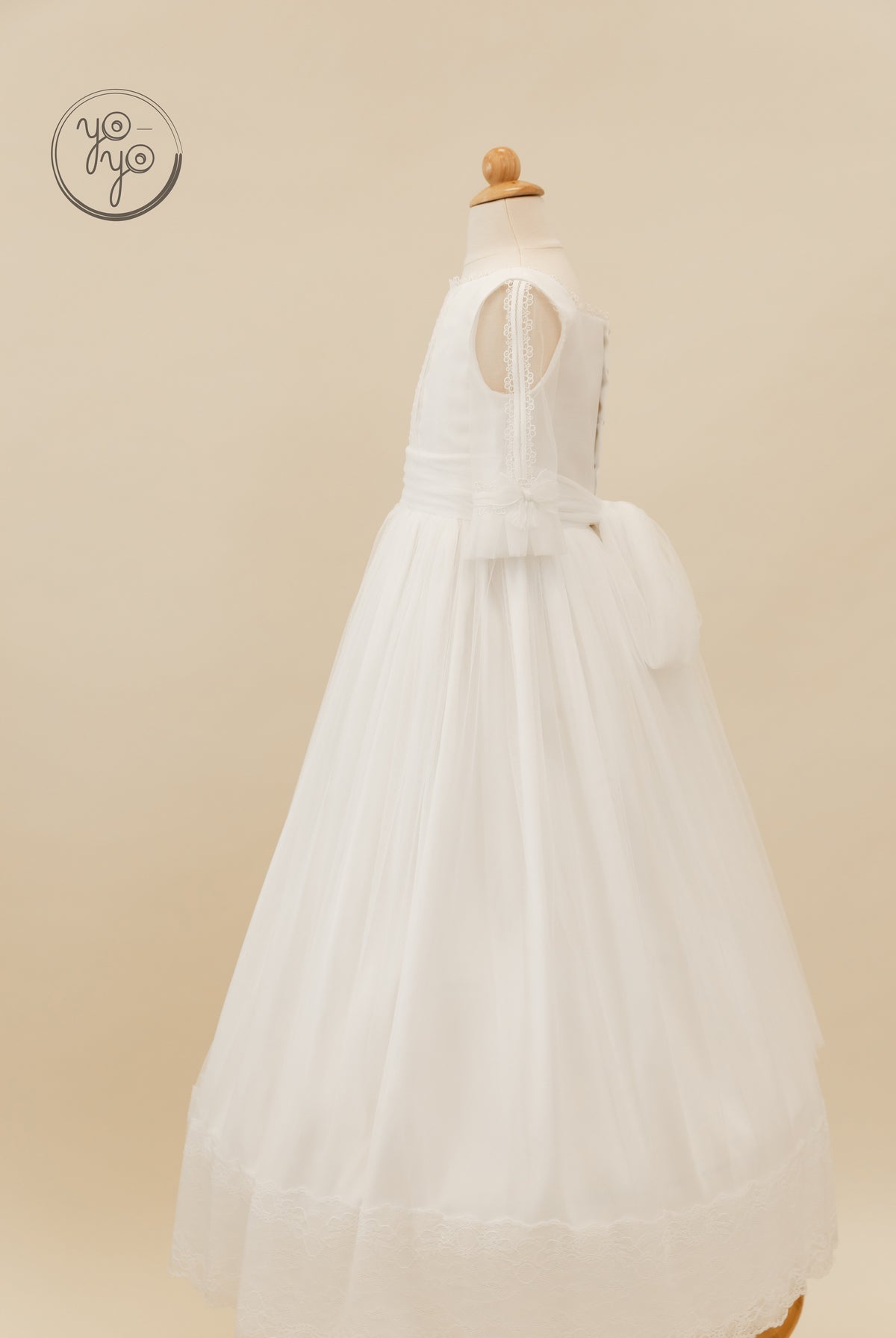Side view of the white Valeriana dress in French tulle, featuring a sheer overlay, lace hem, and a large bow at the back waist.