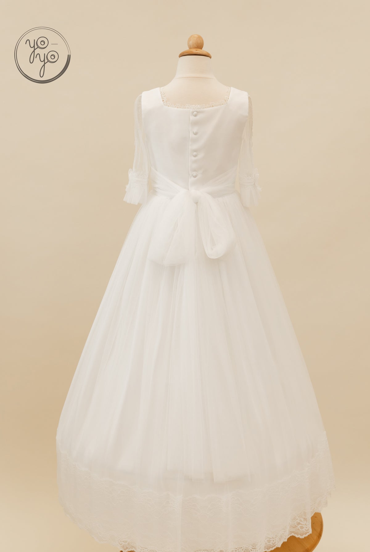 Back view of the white Valeriana Dress, showing sheer sleeves, a buttoned bodice, waist tie, and a lace-trimmed French tulle skirt.