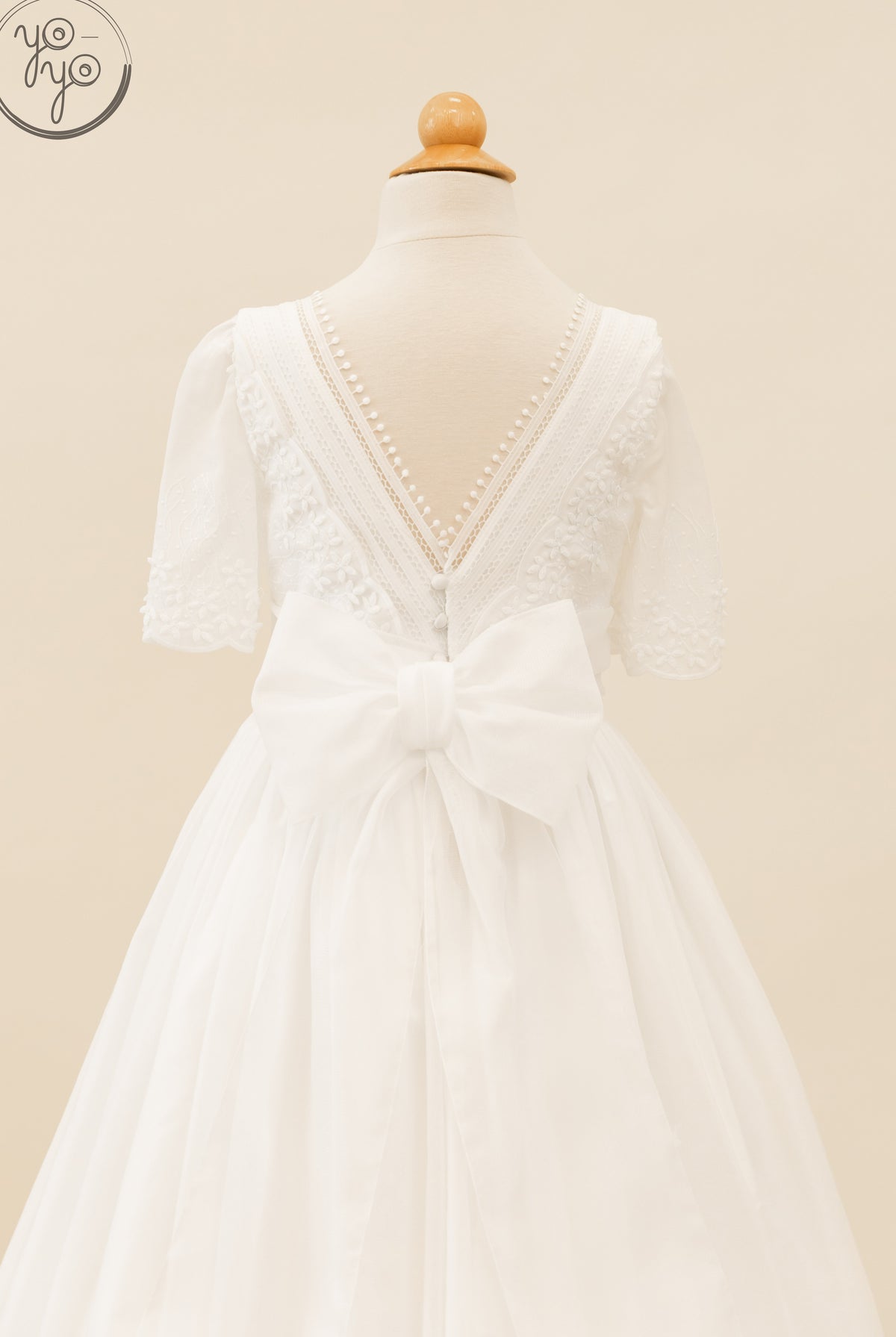 Back view of the white, boho-chic Salvia Dress featuring short sleeves, lace trim, decorative buttons, and a large waist bow.