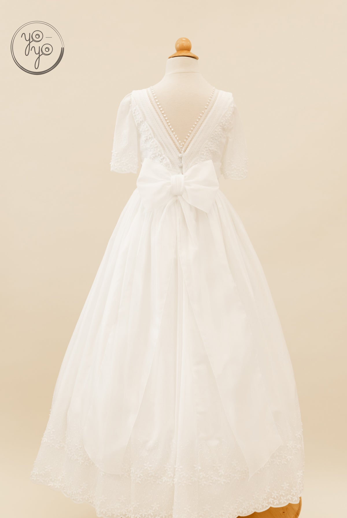 Back view of the white Salvia Dress by YoYo Boutique, featuring a lace-trimmed V-back, decorative buttons, and a large waist bow.